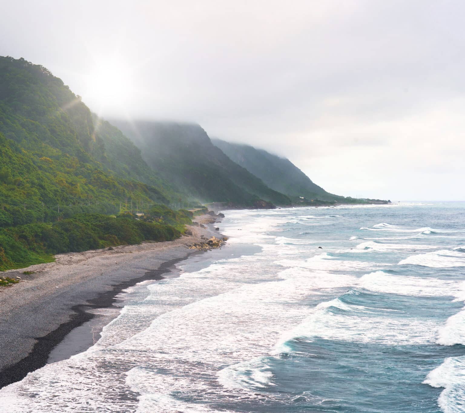 Grüne Bäume führen über einen Strand ins wunderschöne wellige Meer.