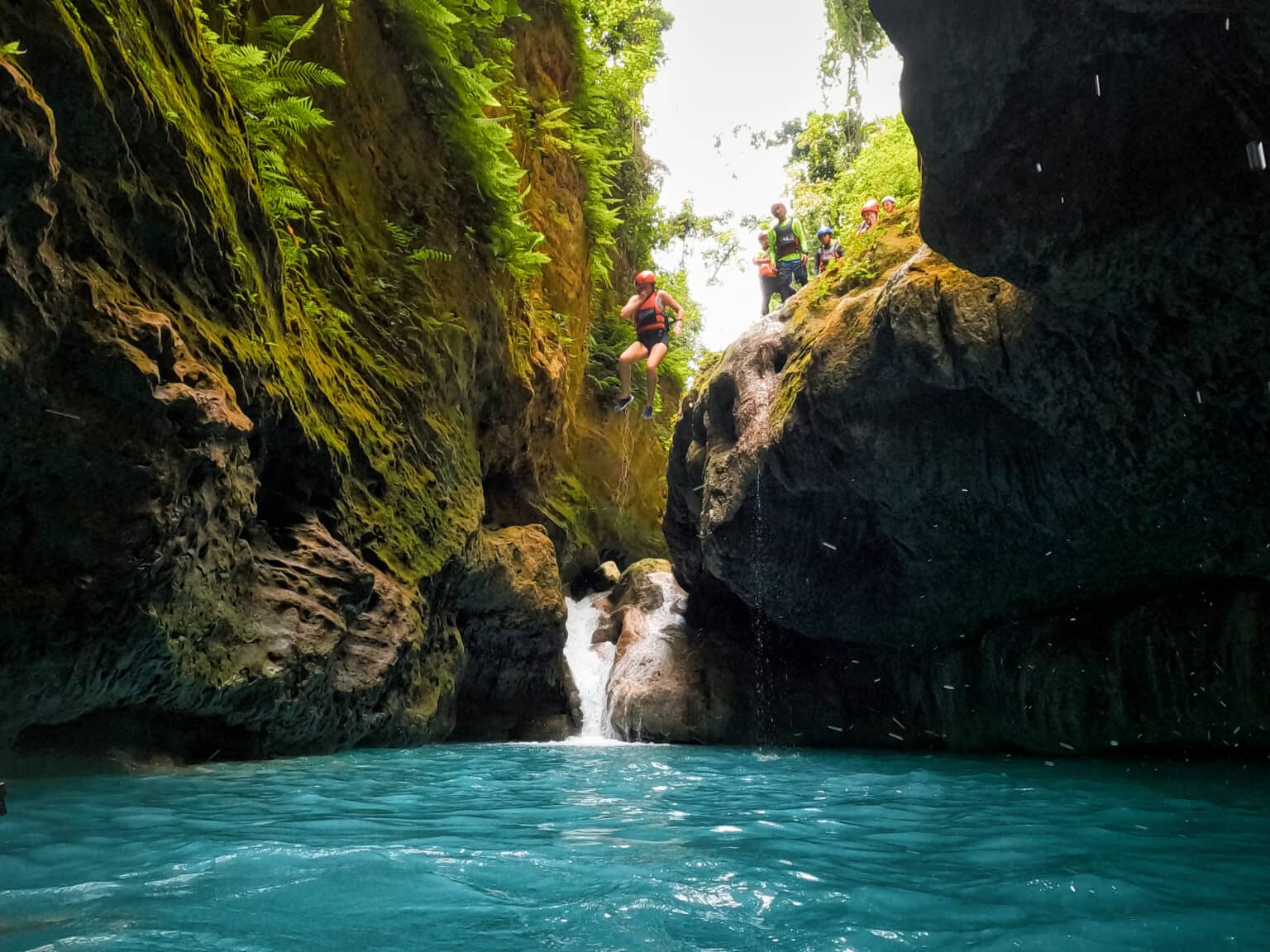 Menschen mit Helmen und Schwimmweste springen in das Türkisblaue Wasser der Schlucht.