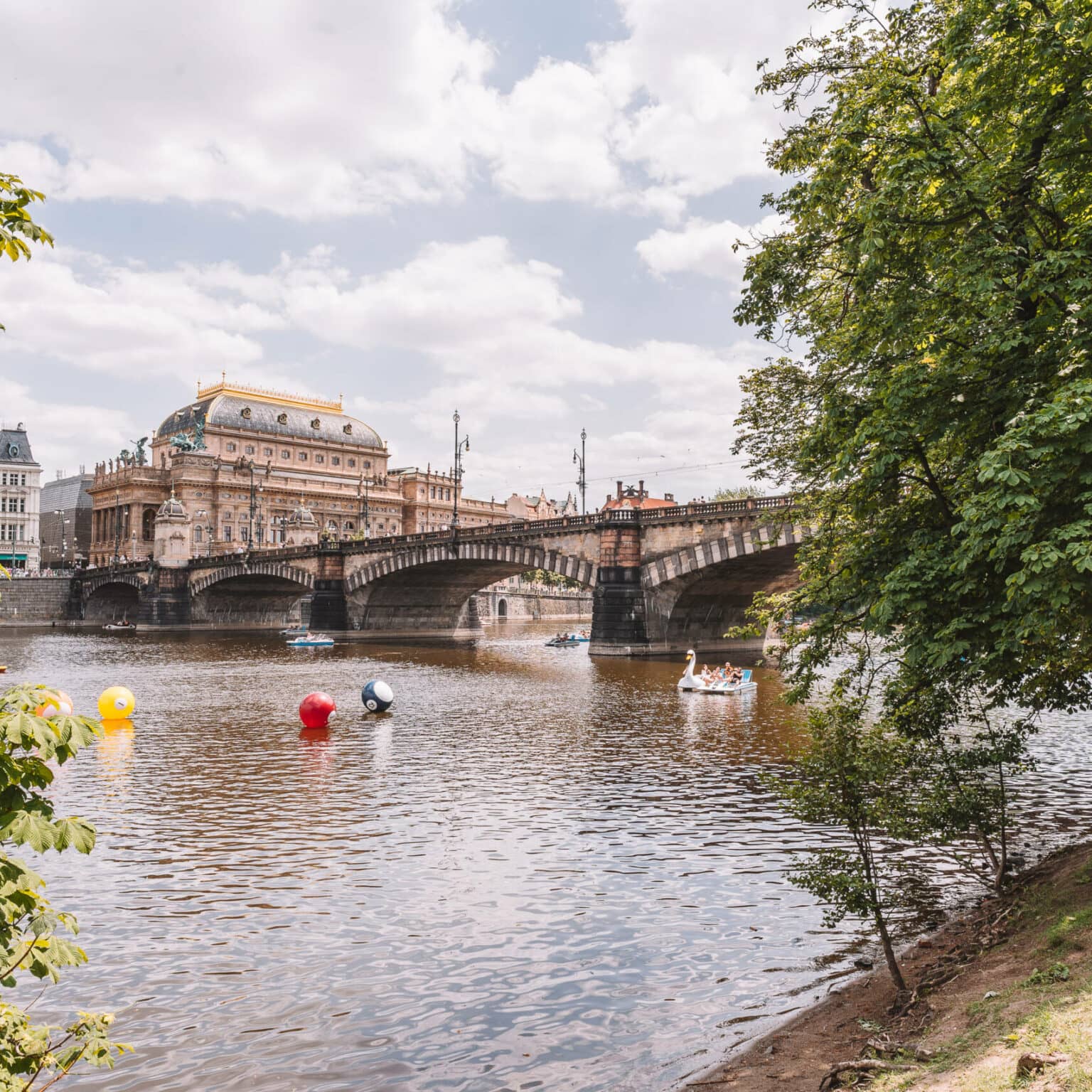 Blick vom Ufer der Moldau auf eine Brück und Gebäude in Prag.