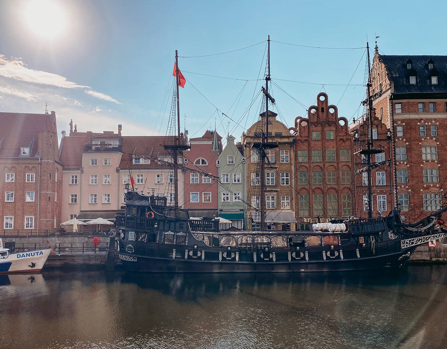 Ein altes Schiff steht im Wasser vor schönen, alten Reihenhäusern.