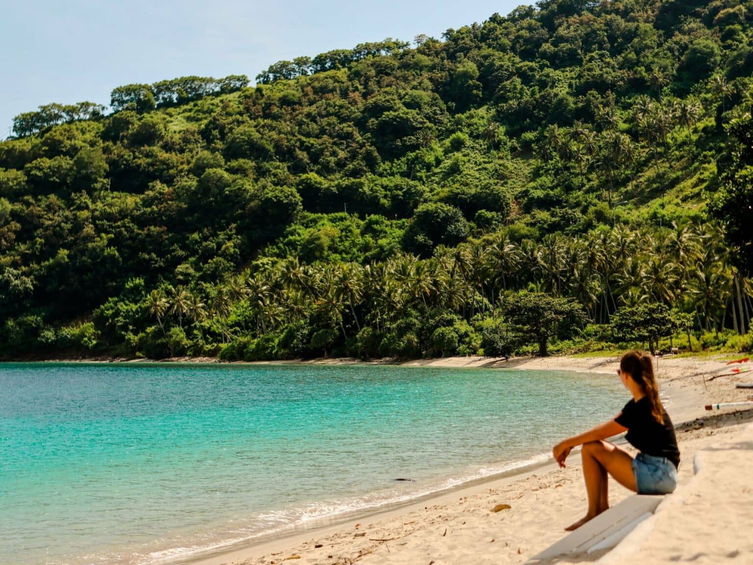Reisebloggerin Nina von Traveloptimizer genießt an einem Sandstrand von Lombok den Blick auf das türkisblaue Meer.