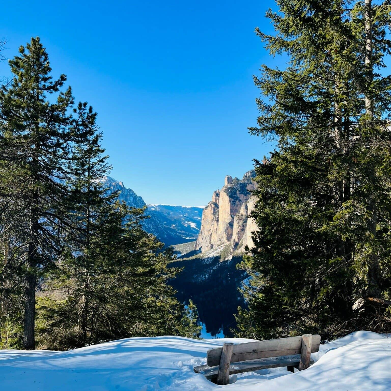 Eine Aussichtsbank im Tiefschnee vor beeindruckender Bergkulisse in den Dolomiten.