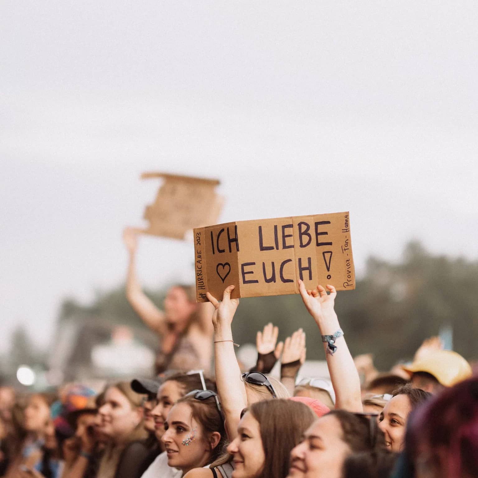 Zuschauer bei einem Konzert mit einem Papierschild in der Hand auf dem "Ich liebe euch" steht.