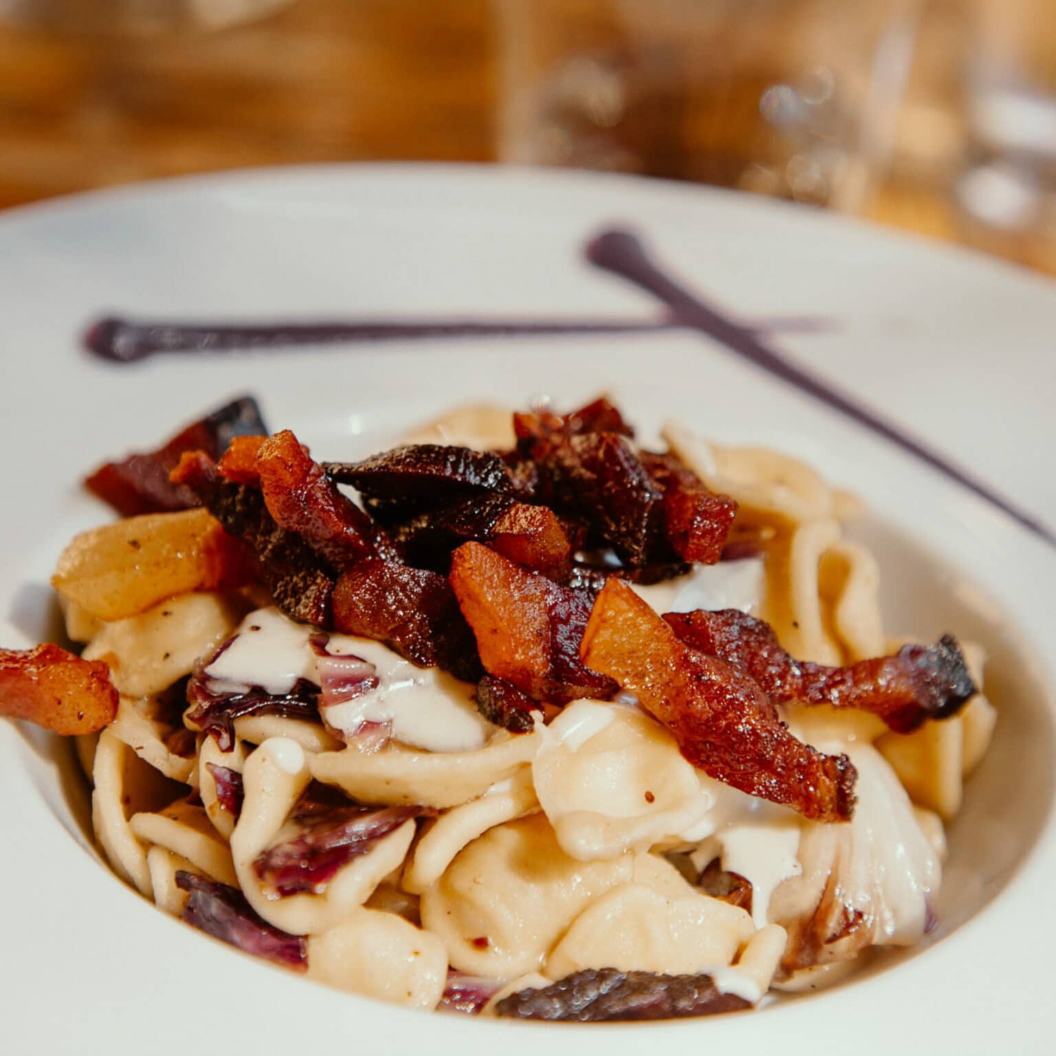 Ein Teller auf dem Pasta zu sehen ist mit Speck oben drauf.