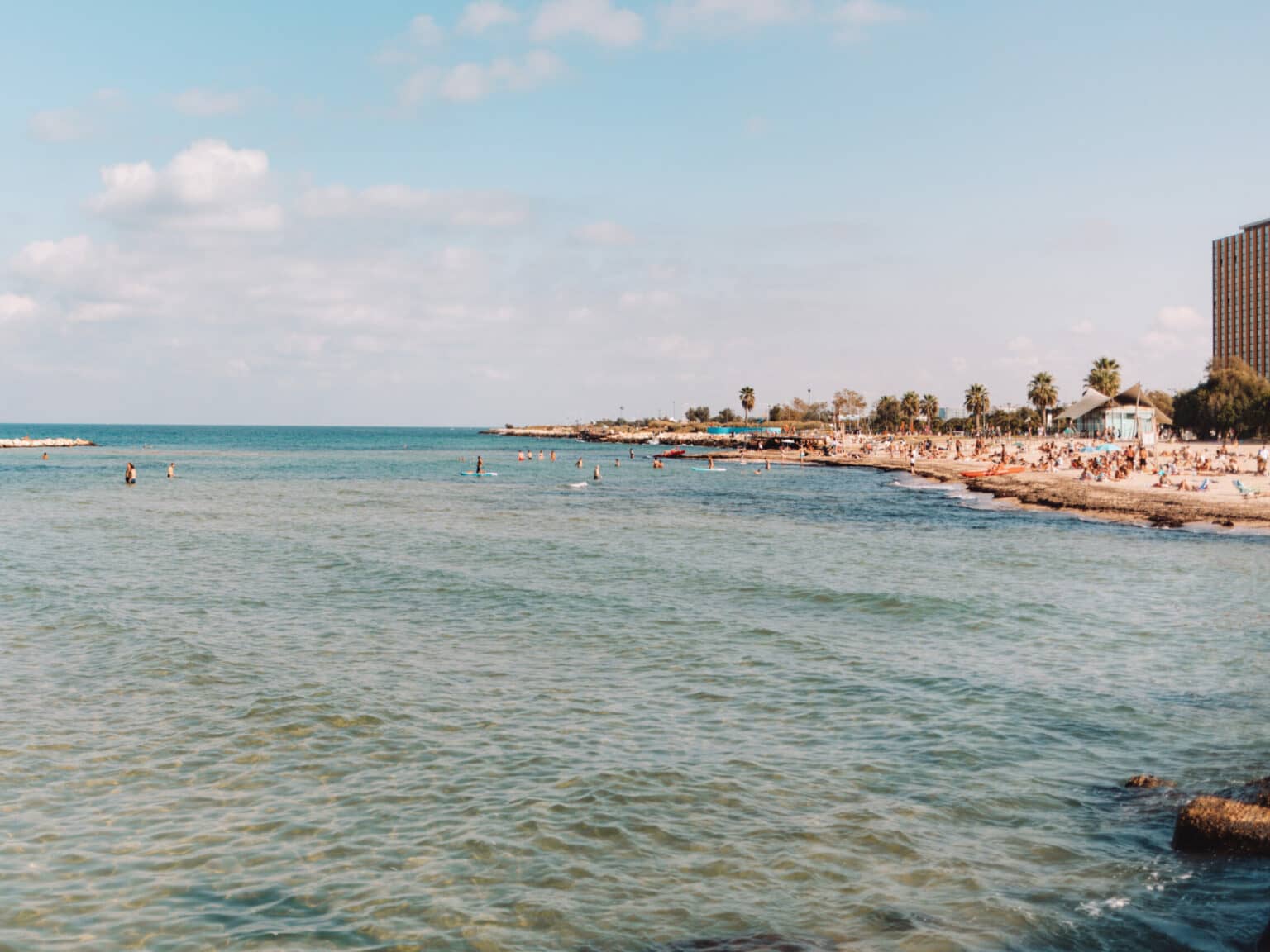 Türkisblaues Wasser am Strand Spiaggia Pane e Pomodoro, im Hintergrund Palmen und Gebäude.