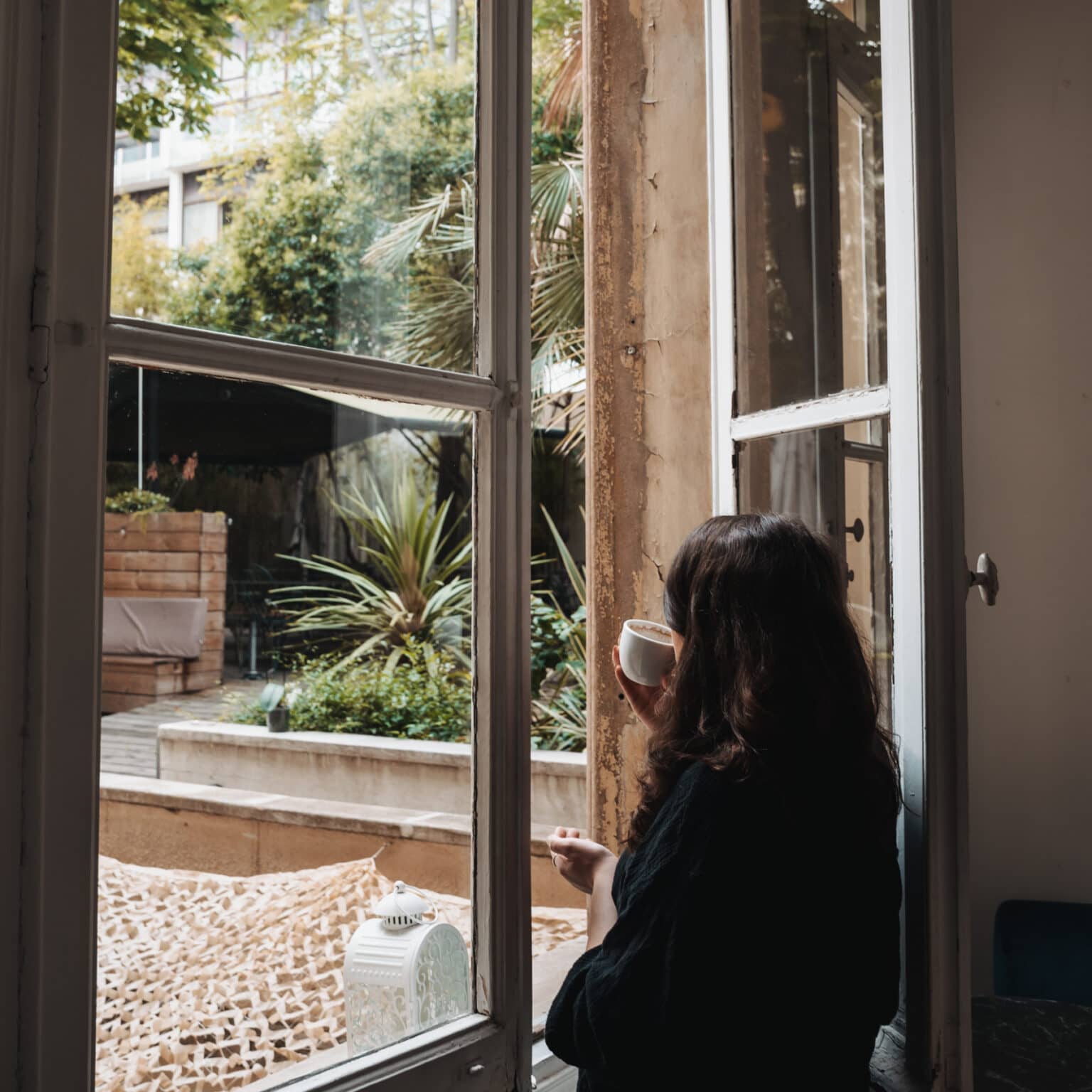 Bloggerin Laura schaut aus dem geöffneten Fenster und hat eine Tasse Kaffee im Hand.