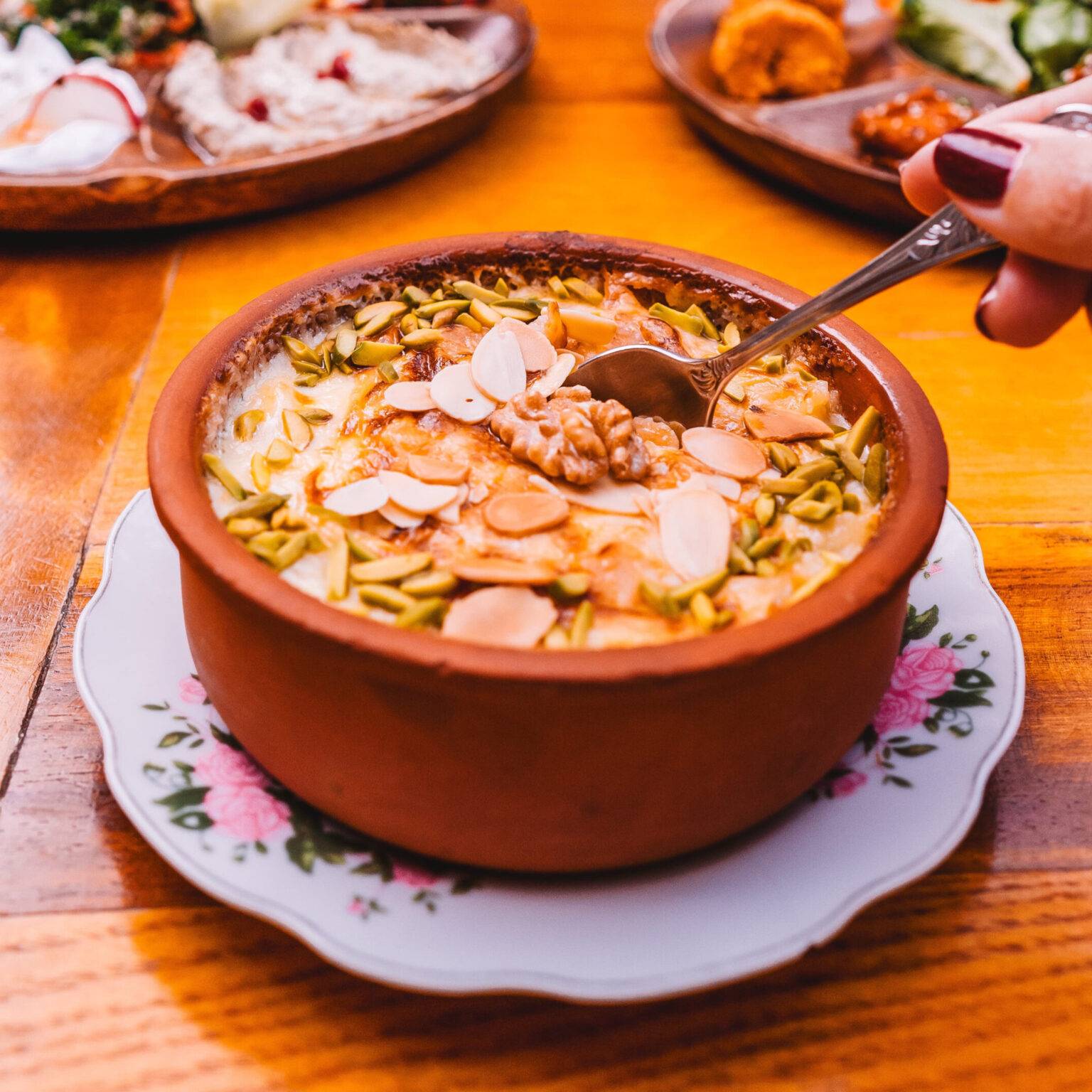 Das arabische Dessert Umm Ali mit Mandelsplittern und Pistazien in einer Tonschale.