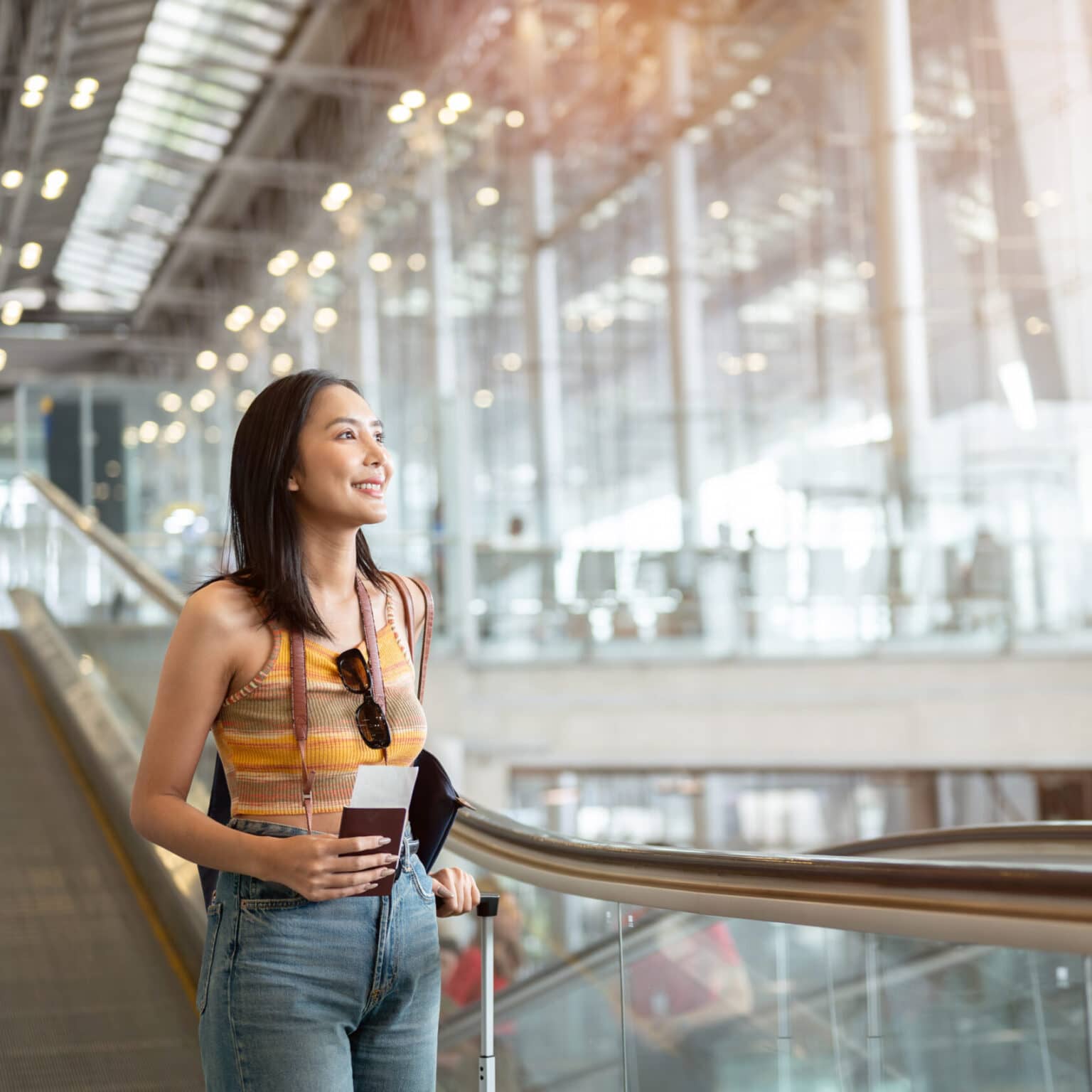 Eine Frau steht mit ihrem Koffer und ihrem Reisepass in der Hand auf einer Rolltreppe am Flughafen.