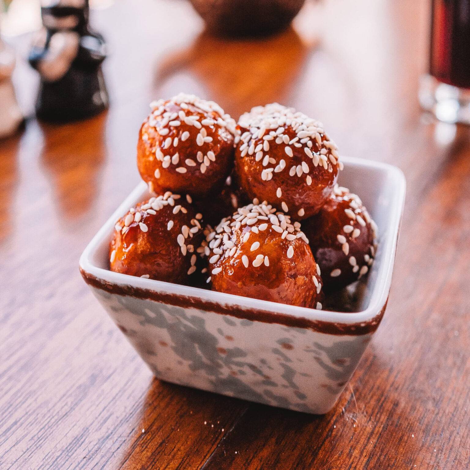 Eine Schale gefüllt mit Lokma, frittierten Teigbällchen, überzogen mit Dattelsirup und bestreut mit Sesamkörnern.