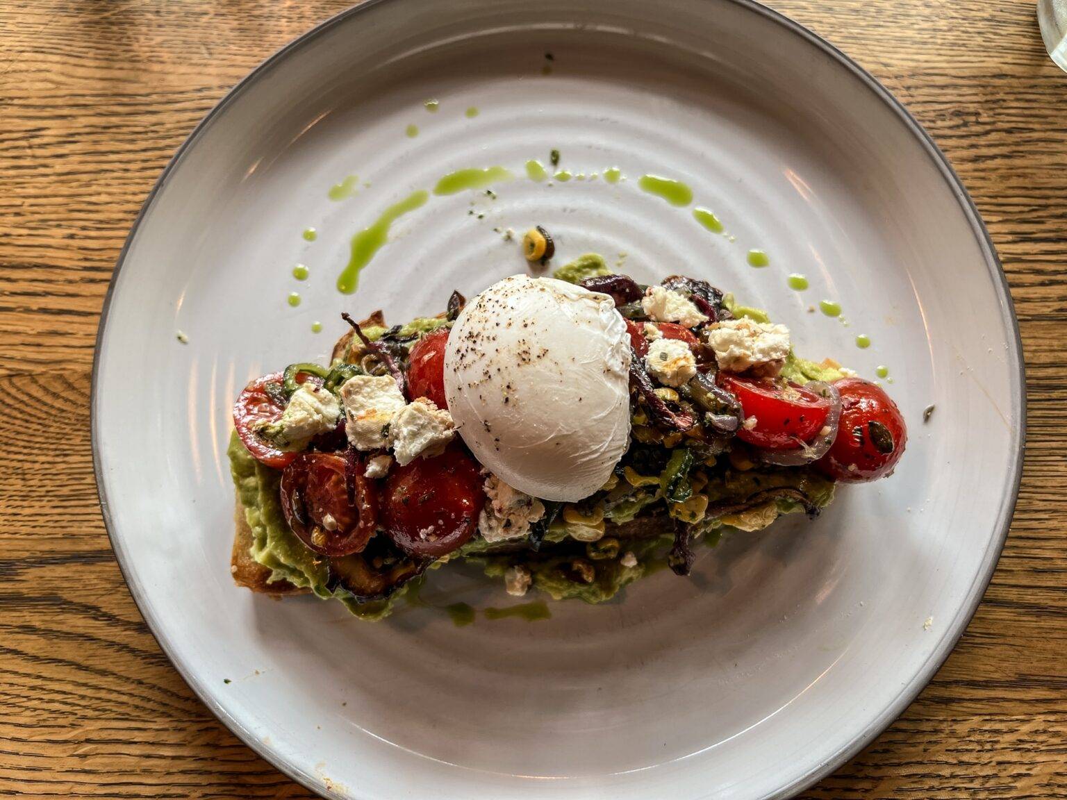 Ein Teller mit einem Smashed Avocado Toast getoppt mit Tomaten und einem Ei.