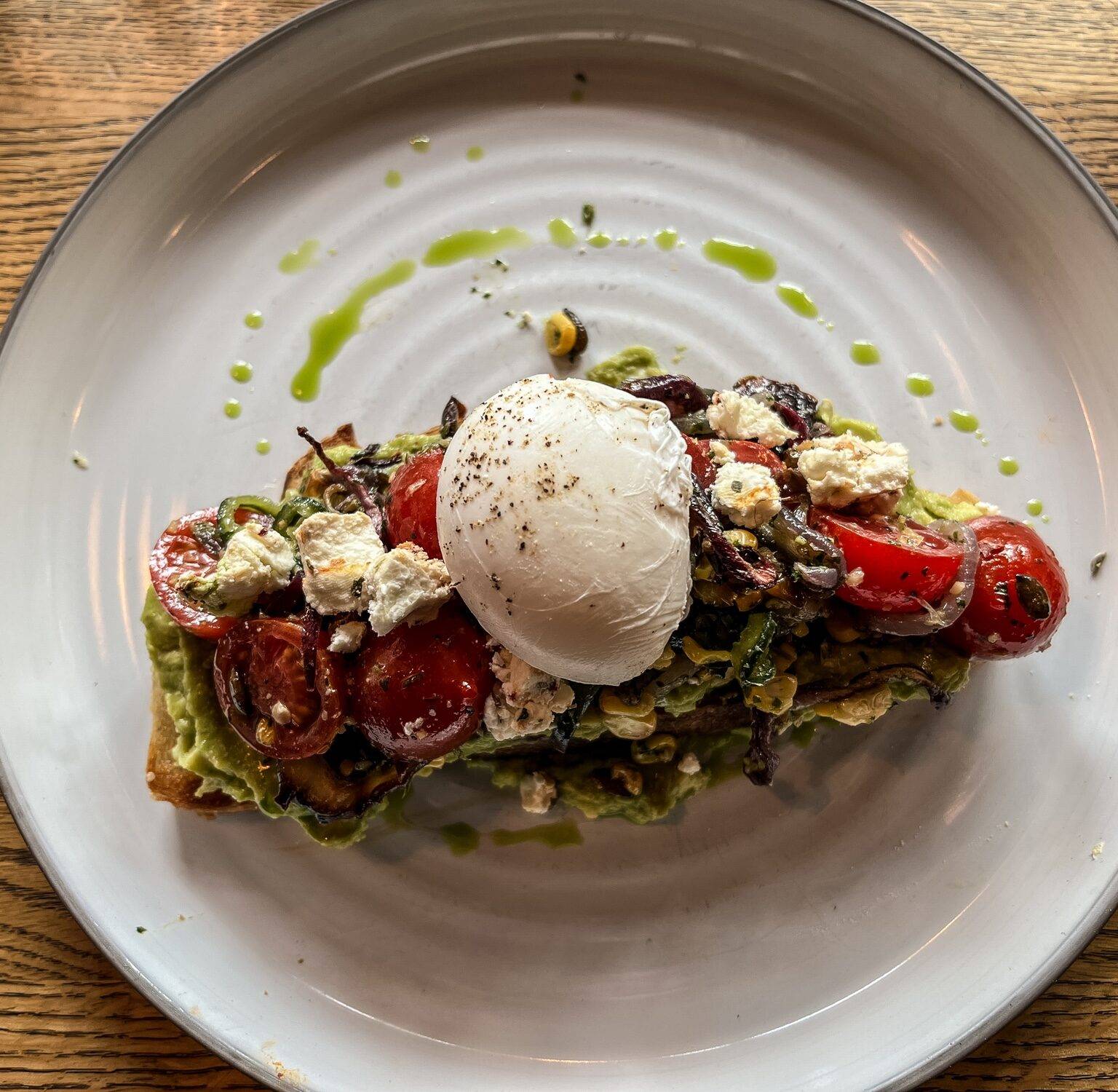 Ein Teller mit einem Smashed Avocado Toast getoppt mit Tomaten und einem Ei.