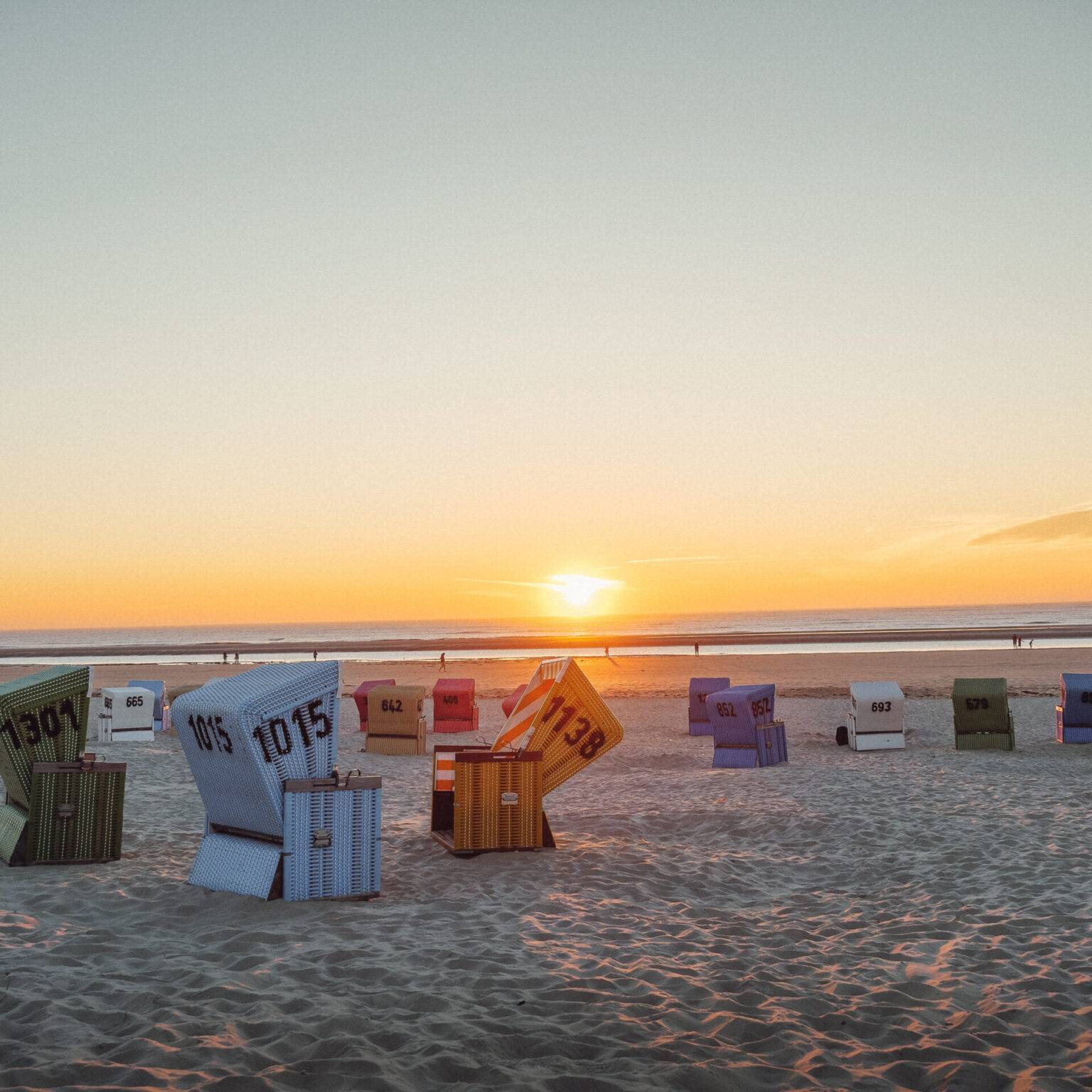 Ein Strand auf Langeoog mit vielen bunten Strandkörben bei Sonnenuntergang.