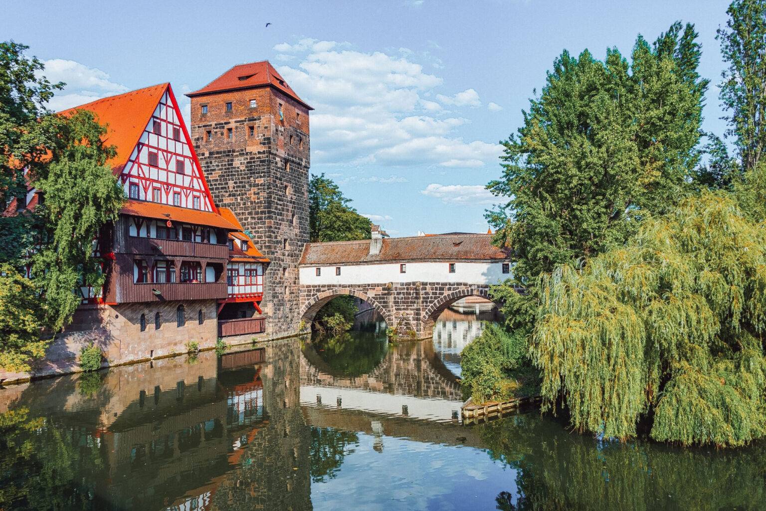 Die Henkerbrücke in Nürnberg, eine aus Steinen gemauerte, überdachte Brücke über die Pegnitz mit einem Turm und einem Fachwerkhaus auf der linken Seite.