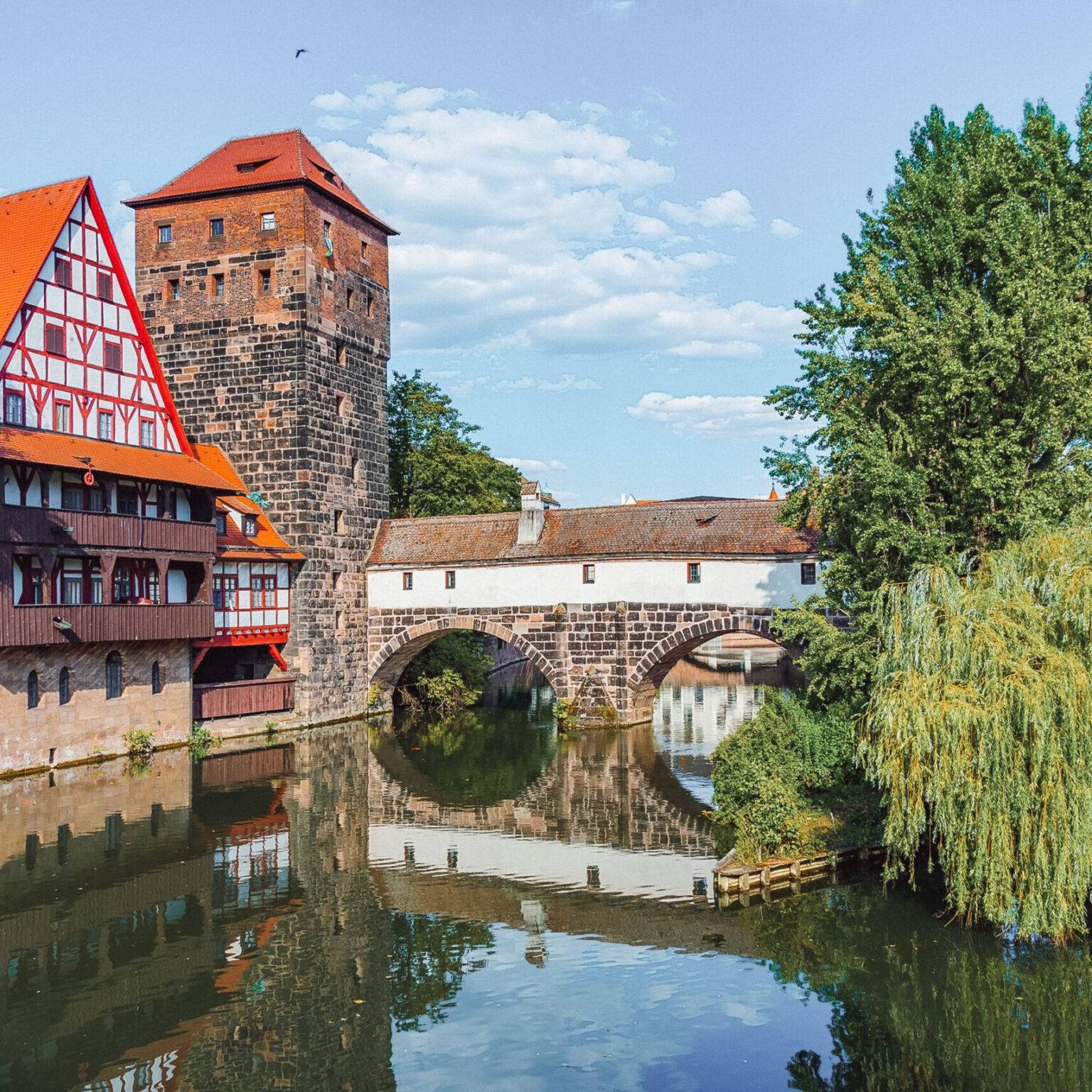 Die Henkerbrücke in Nürnberg, eine aus Steinen gemauerte, überdachte Brücke über die Pegnitz mit einem Turm und einem Fachwerkhaus auf der linken Seite.