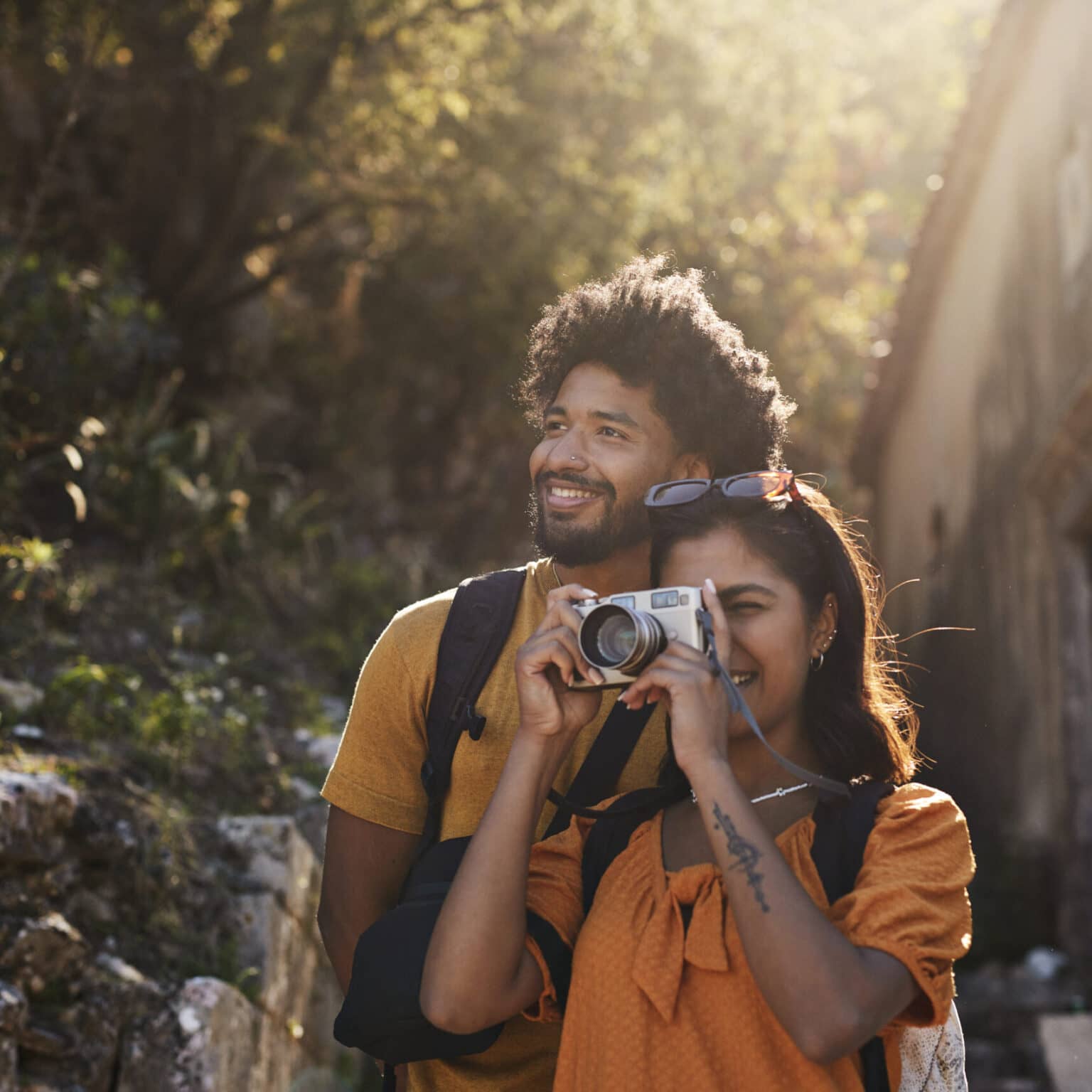 Ein Mann und eine Frau stehen draußen im Grünen. Sie fotografiert mit einer Kamera.