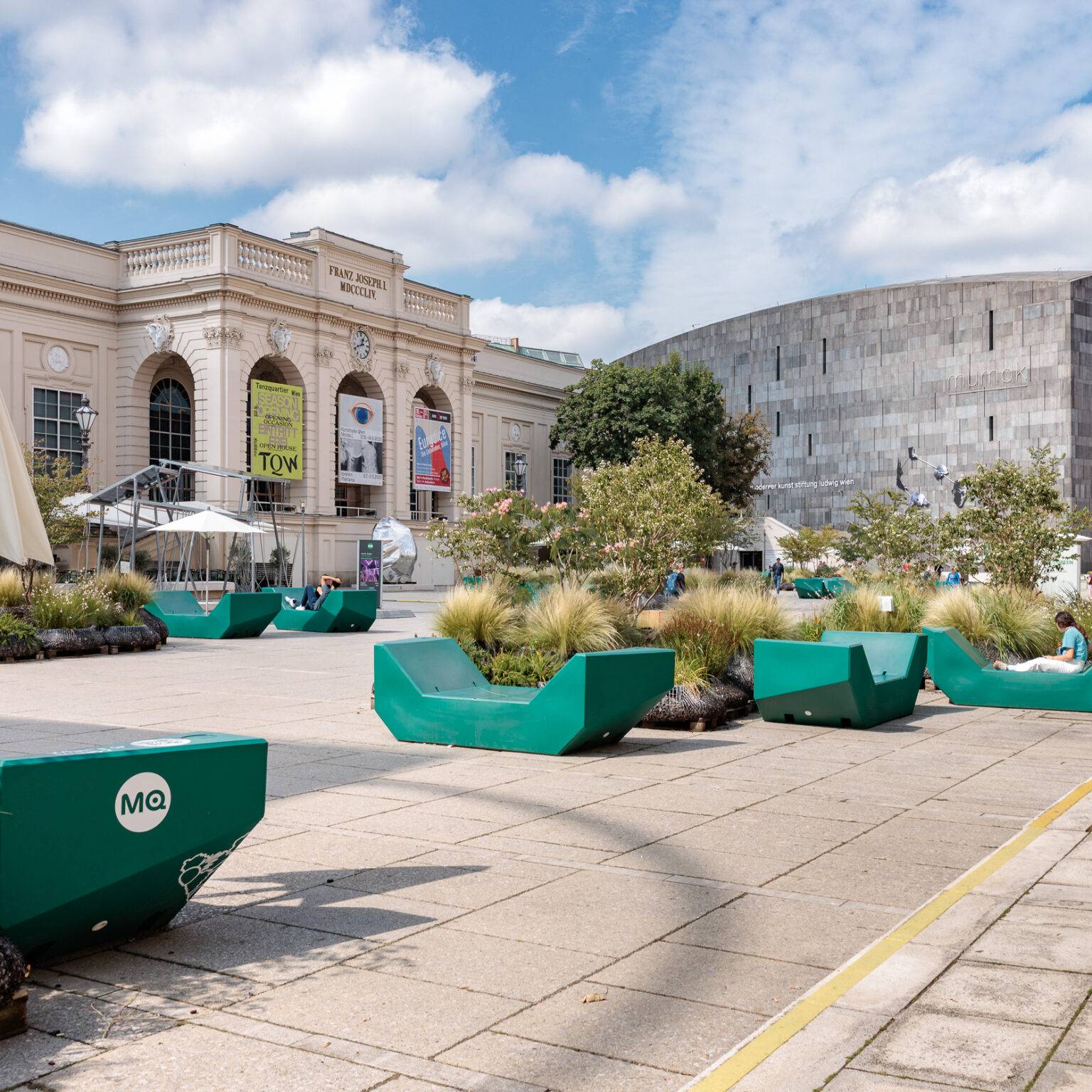 Innenhof des MuseumsQuartiers mit grünen "Enzis", Pflanzkübeln, einem klassischen und einem modernen Gebäuden im Hintergrund und blauen Himmel.