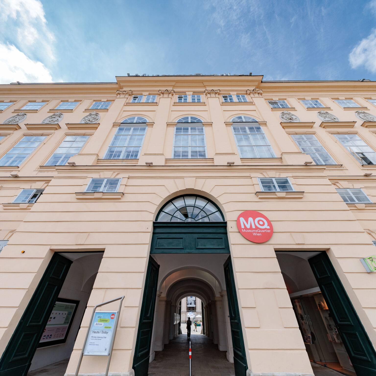 Klassische Fassade MuseumsQuar mit großen Fenstern und einem zentralen Torbogen, unter blauem Himmel.