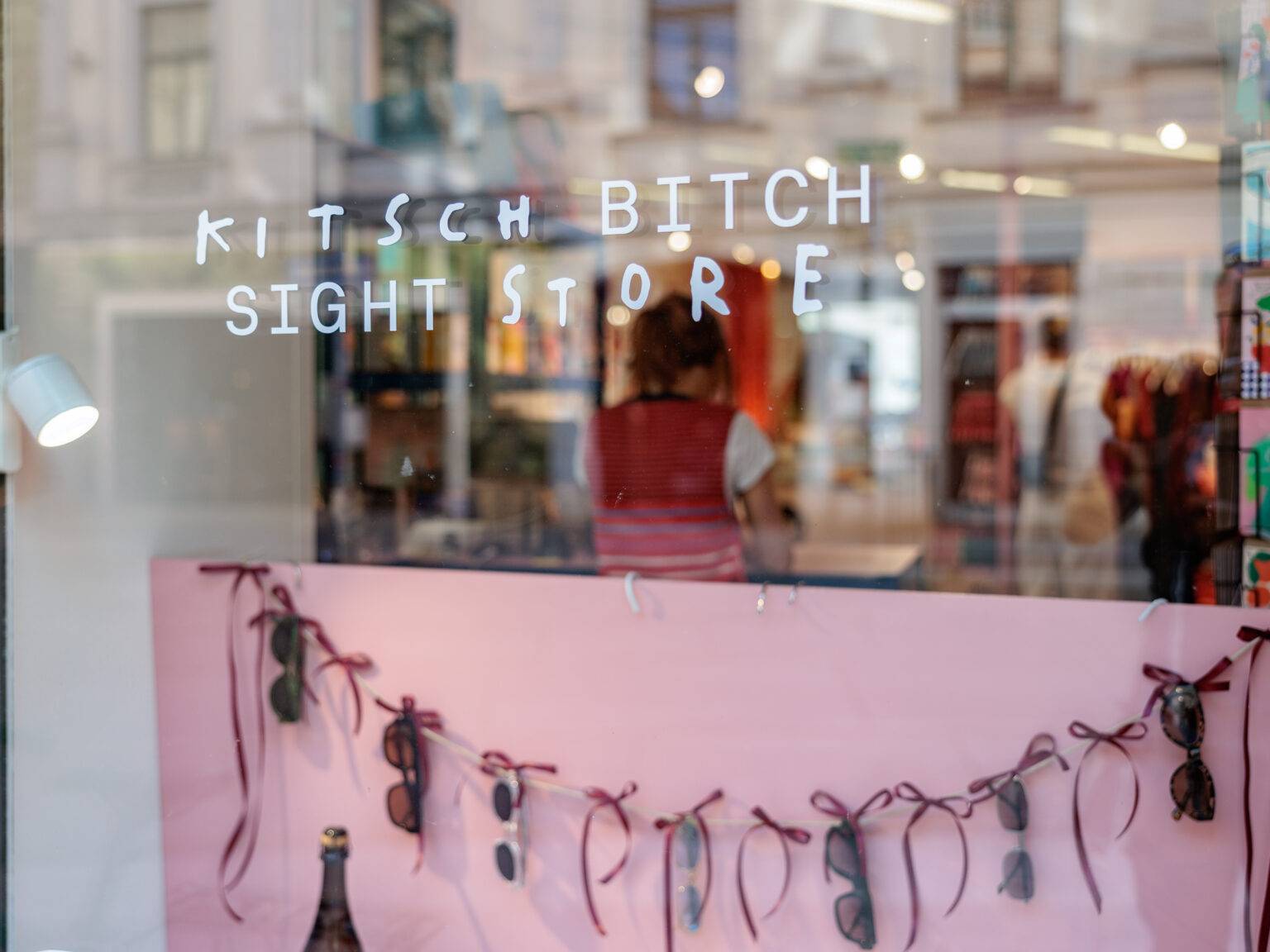 Schaufenster mit dem Schriftzug "KITSCH BITCH SIGHT STORE" und einer Girlande aus Sonnenbrillen.