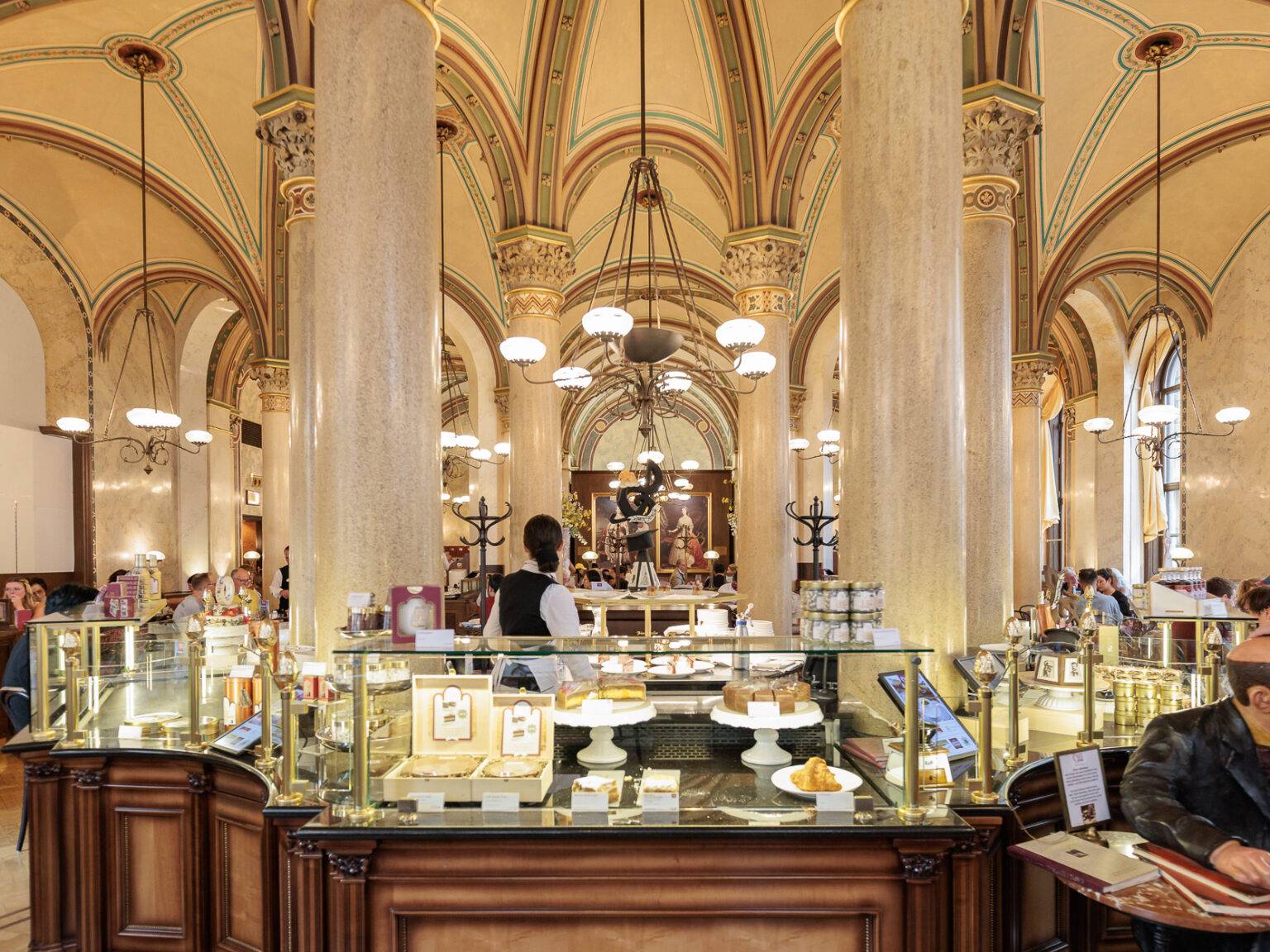 Eleganter Innenbereich des Café Central mit hohen Säulen, kunstvollem Deckenmuster und einer Theke voller Gebäck.