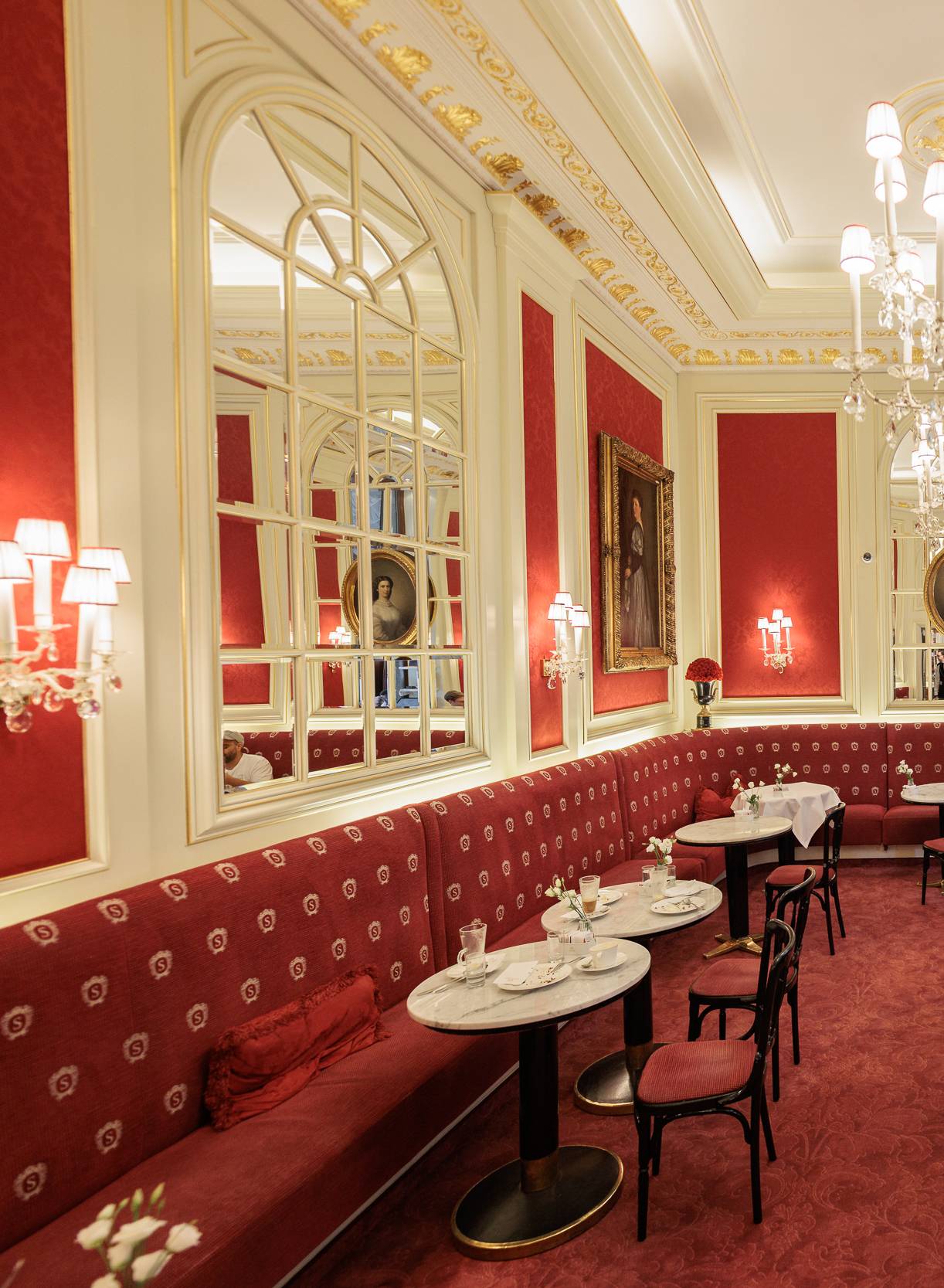 Das Kaffeehaus Sacher von innen mit eleganter, barocker Einrichtung mit roten Wänden, rotem Teppich und Kronleuchtern.