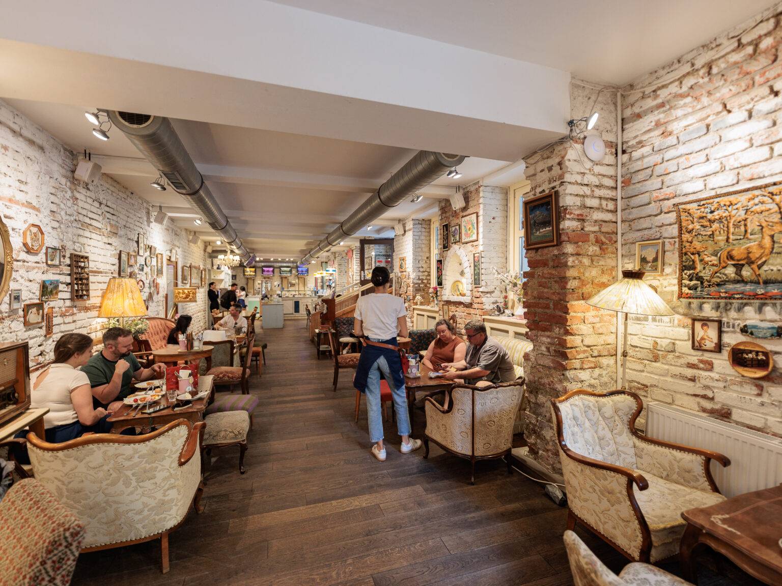 Gemütliches Café Vollpension mit vintage Möbeln, Gästen an Tischen und einer warmen, einladenden Atmosphäre.