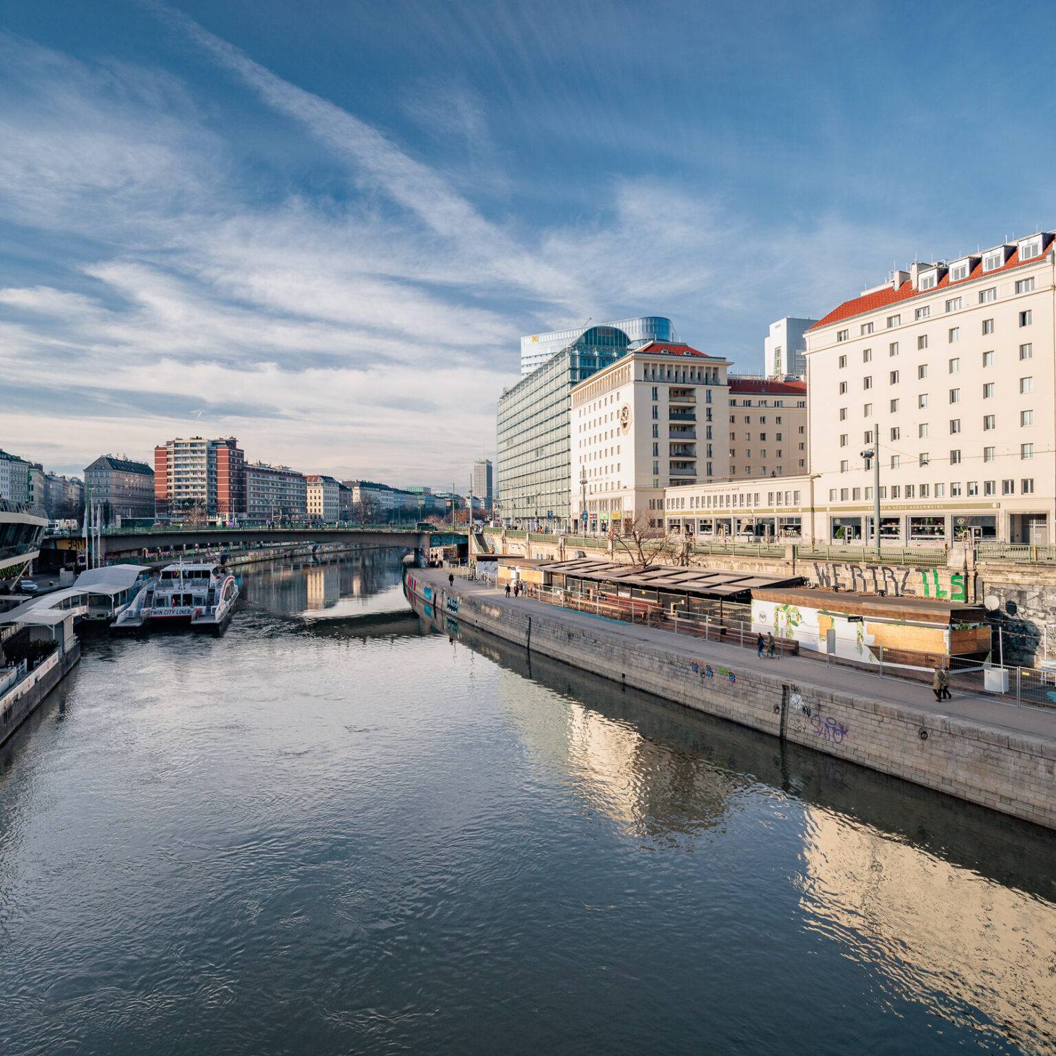 Donaukanal umgeben von modernen Gebäuden und Booten am Ufer.