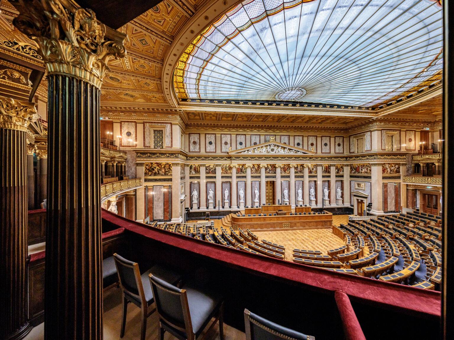 Das prächtige Parlament von Wien von Innen mit goldenen Verzierungen, Säulen und einer großen, gläsernen Kuppel.