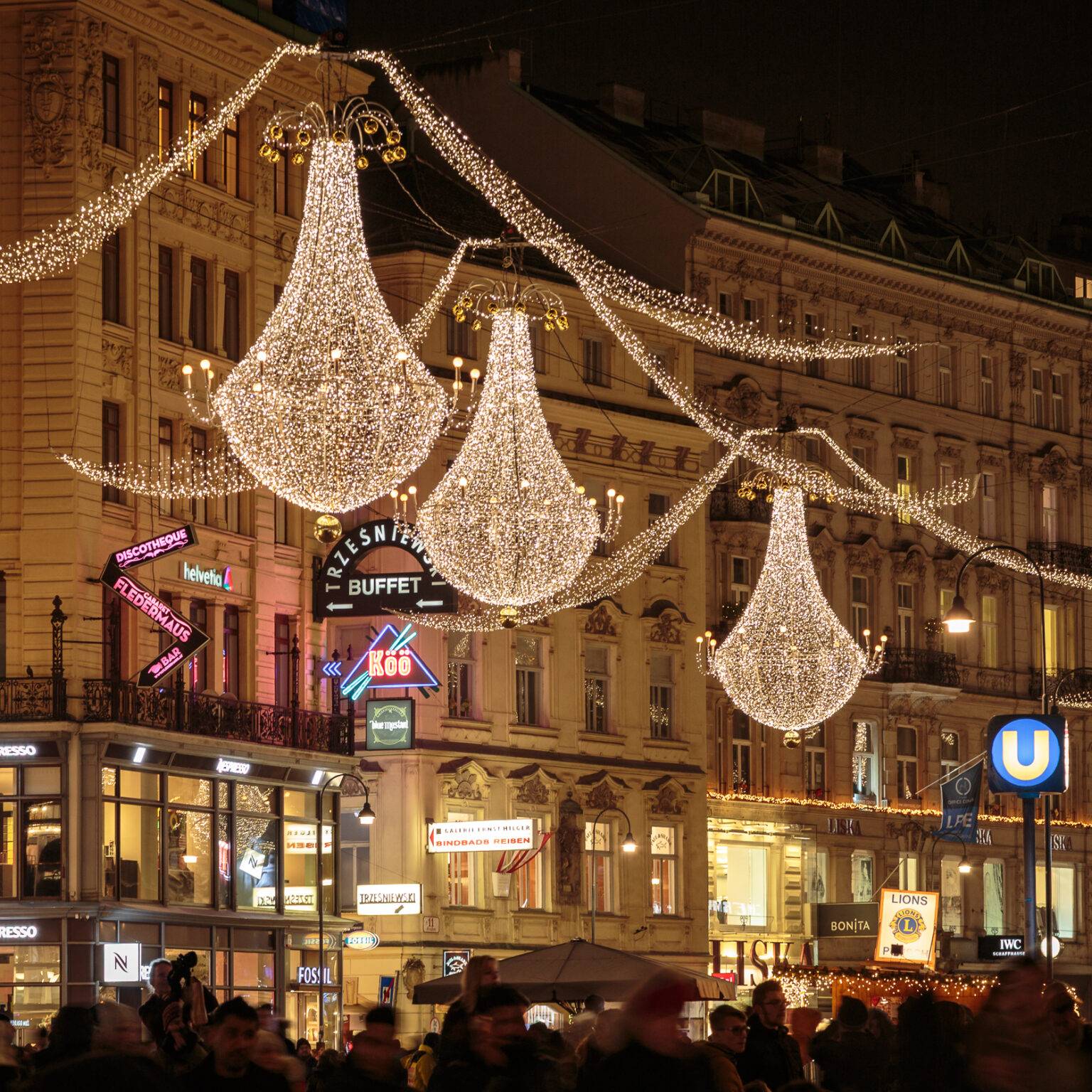 Weihnachtlich beleuchteter Graben in Wien mit festlichen Lichtern und Menschenmengen in einer urbanen Umgebung bei Nacht.