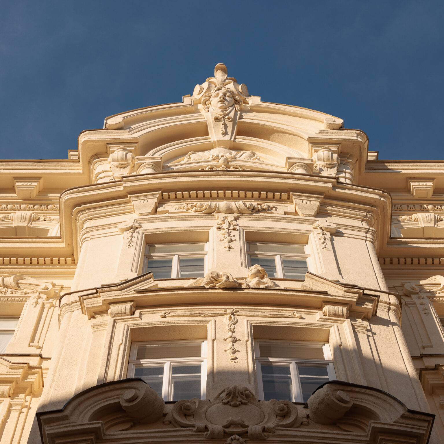 Detailreiche Fassade eines historischen Gebäudes mit Skulpturen und Fenstern, unter blauem Himmel.