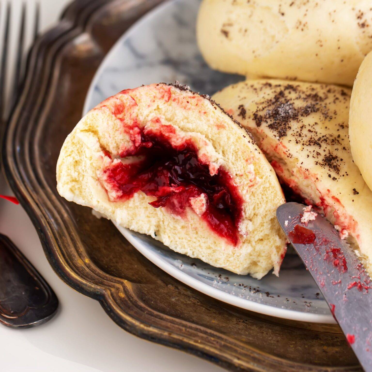 Ein Teller mit Germknödeln, Hefeknödel mit Zwetschkenmus, neben einem Messer und Besteck.