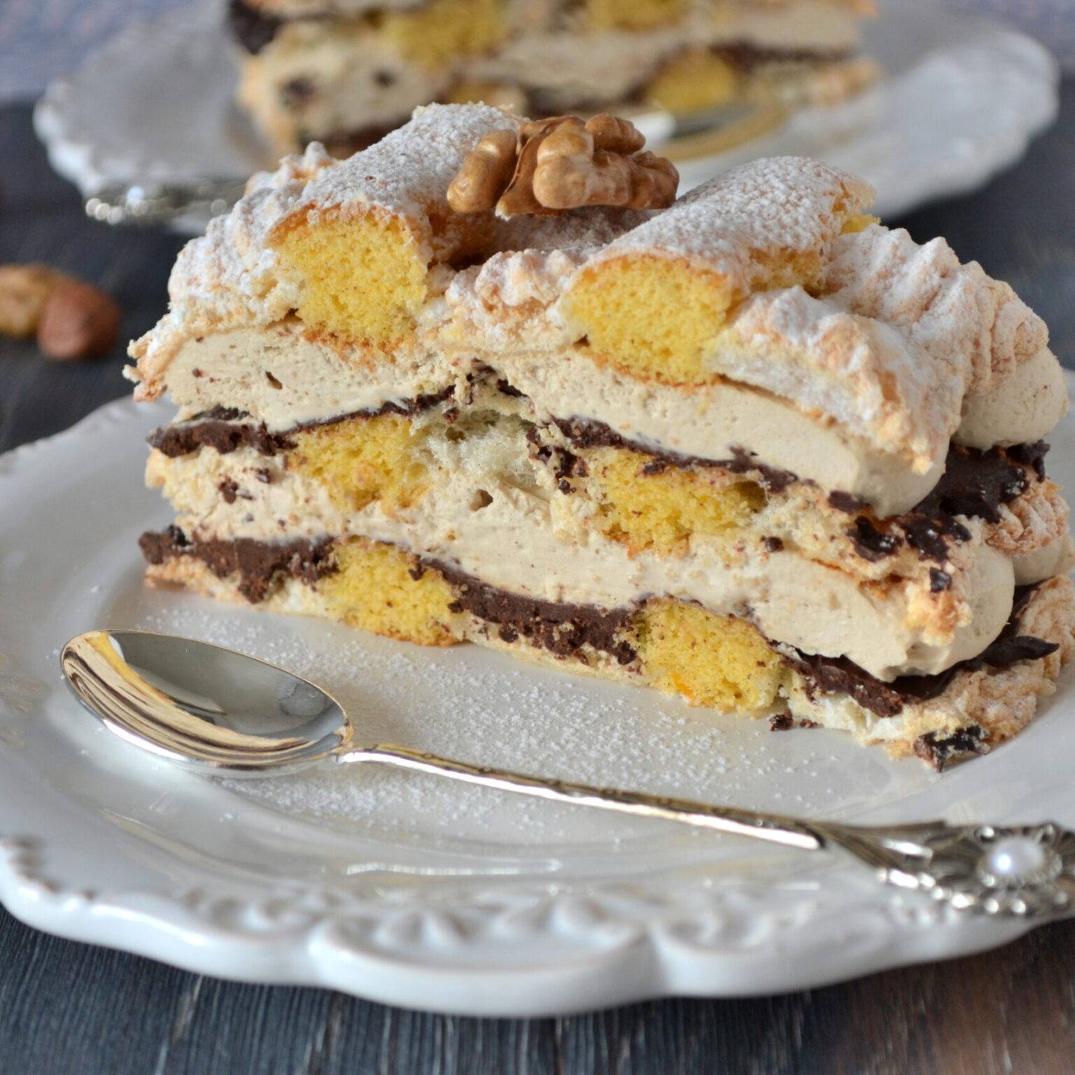 Eine Kardinalschnitte, ein mehrschichtiger Kuchen mit Biskuit, Eischnee und Sahne auf einem weißen Teller.
