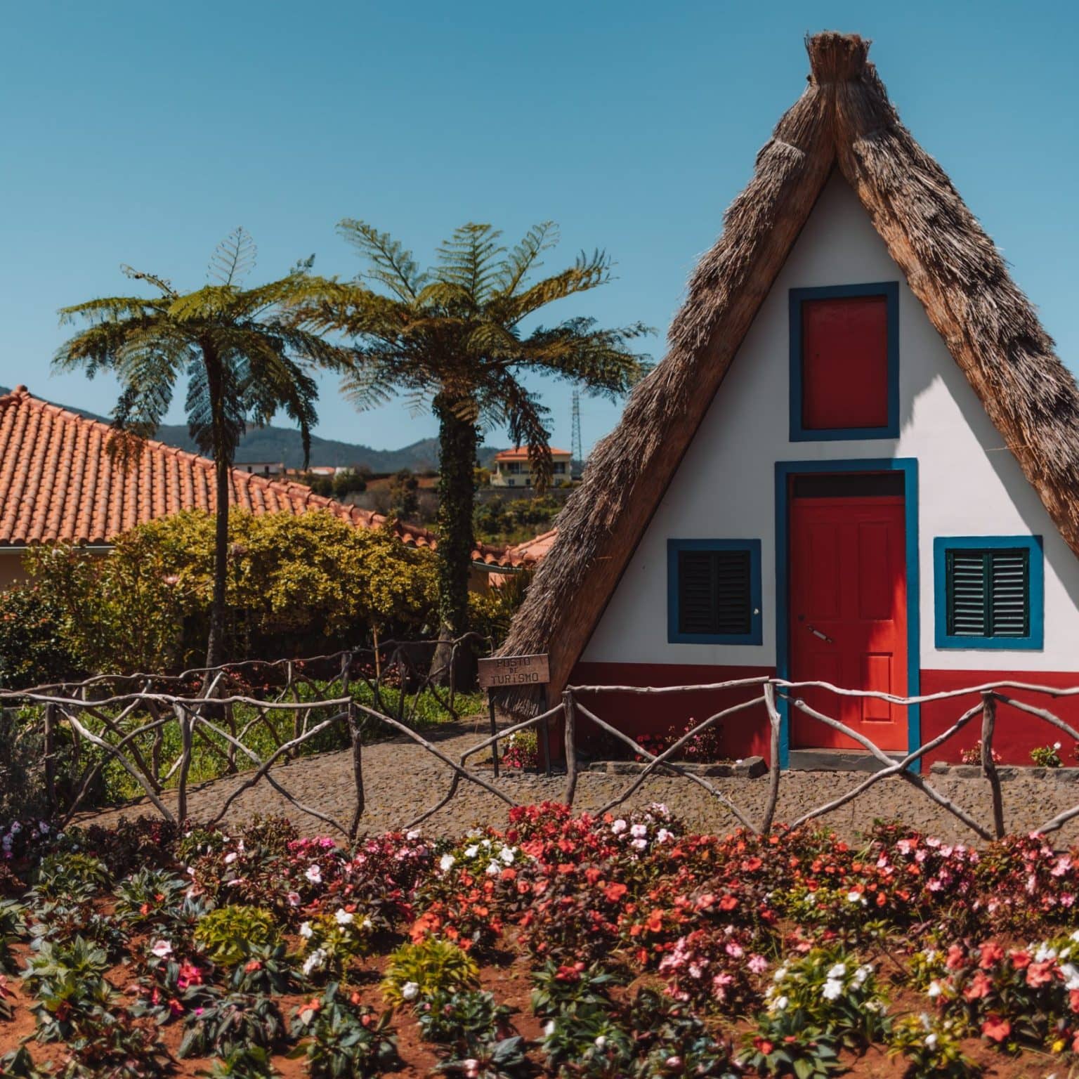 Ein typisches zeltförmiges Haus mit Reetdach ist bunt bemalt hinter einem bunten Blumengarten.