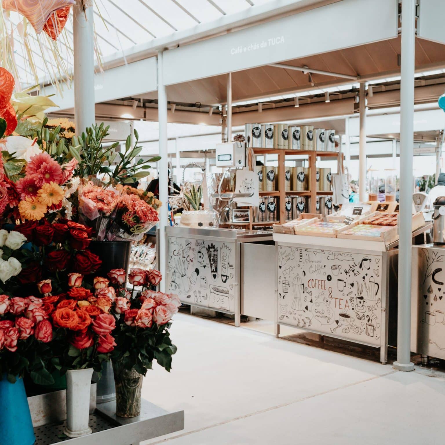 Ein bunter Blumenstand auf einem überdachten Markt, dahinter ein Teestand.