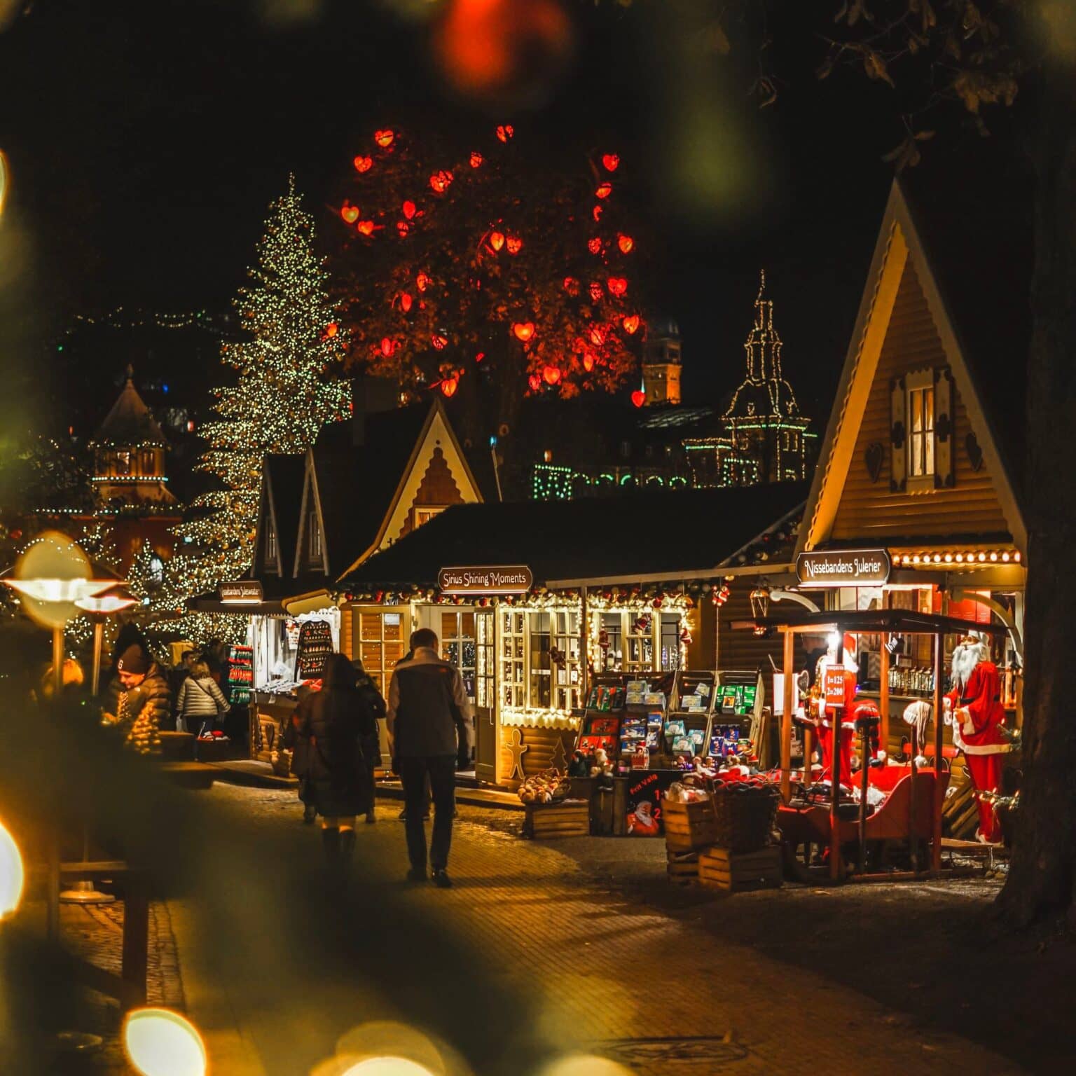Verschiedene Stände auf dem Weihnachtsmarkt im Freizeitpark Tivoli sind bei Nacht mit vielen Lichterketten beleuchtet.