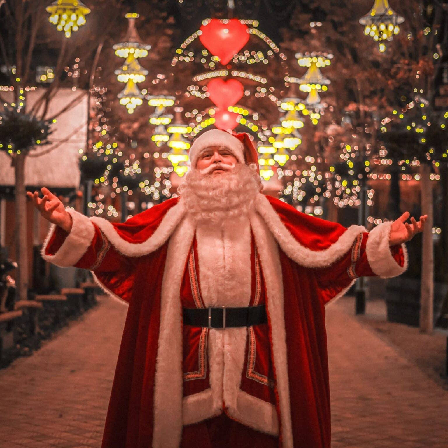 Ein Mann, als Weihnachtsmann verkleidet, steht in einer mit Lichterketten beleuchteten Allee.