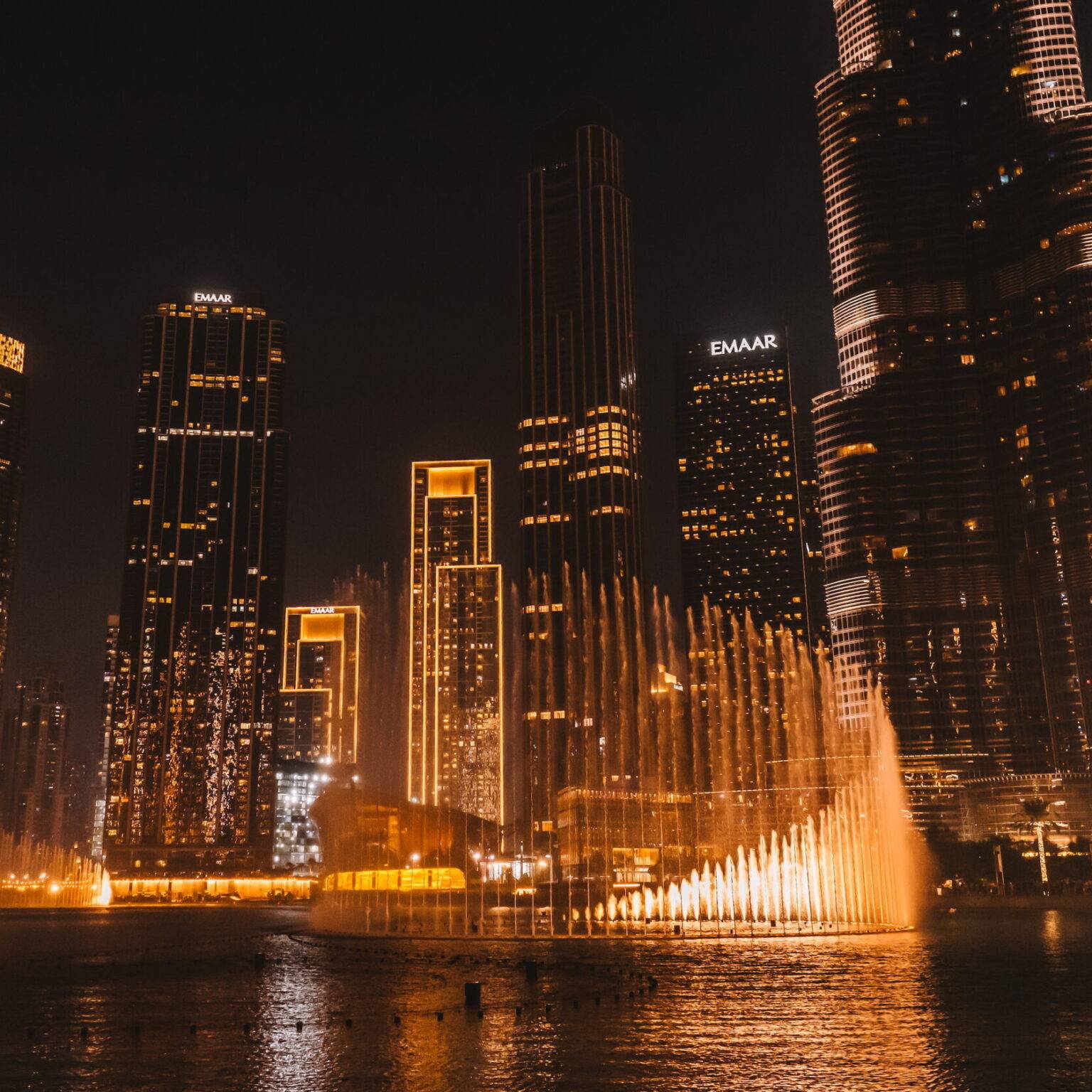 Die Dubai Fountains bei Nacht umgeben von beleuchteten Hochhäusern.