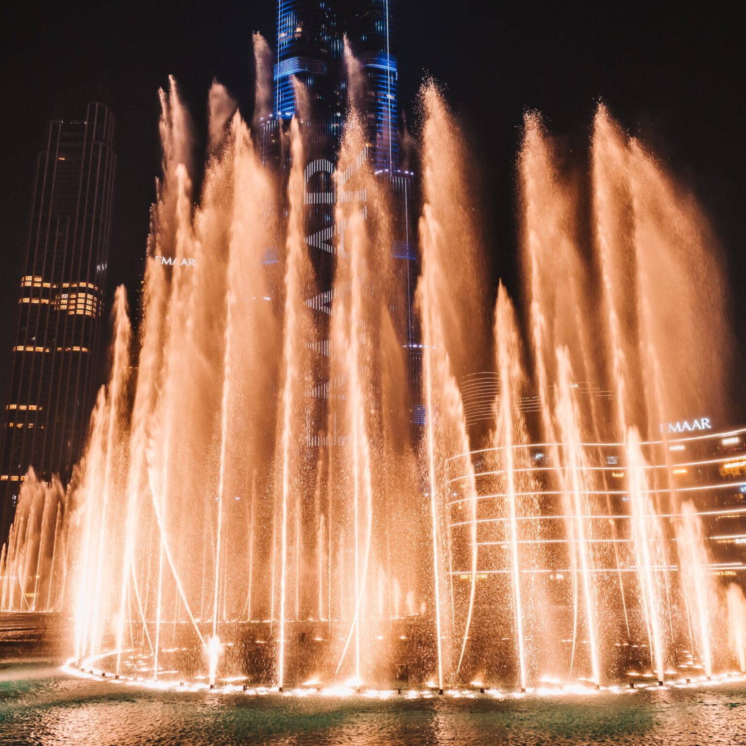 Die Dubai Fountains bei Nacht umgeben von beleuchteten Hochhäusern.