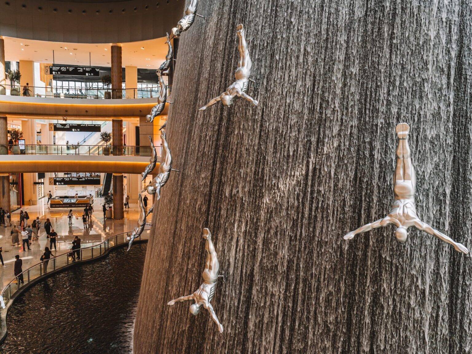 Ein großer, künstlicher Wasserfall in der Dubai Mall durchzogen von silbernen, männlichen Figuren, die kopfüber und mit ausgebreiteten Armen auf dem ganzen Wasserfall angebracht sind.