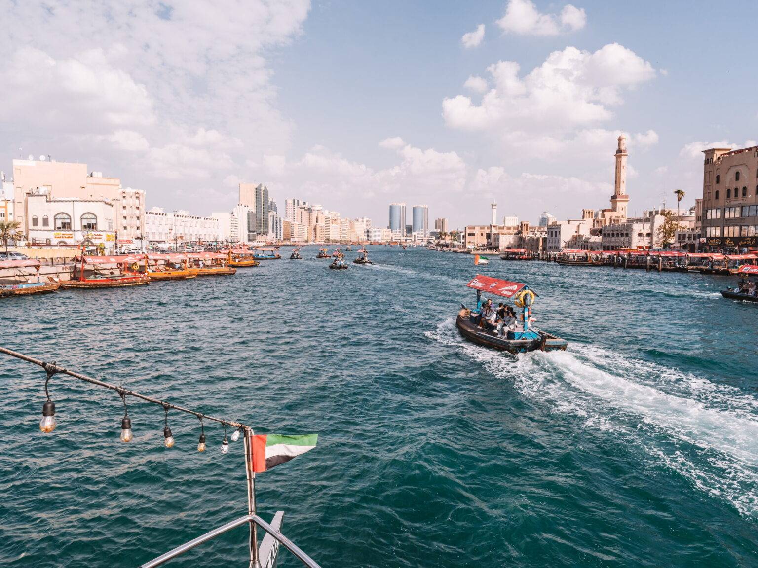 Der Dubai Creek mit vielen kleinen überdachten Booten und vielen Gebäuden links und rechts des Flusses.