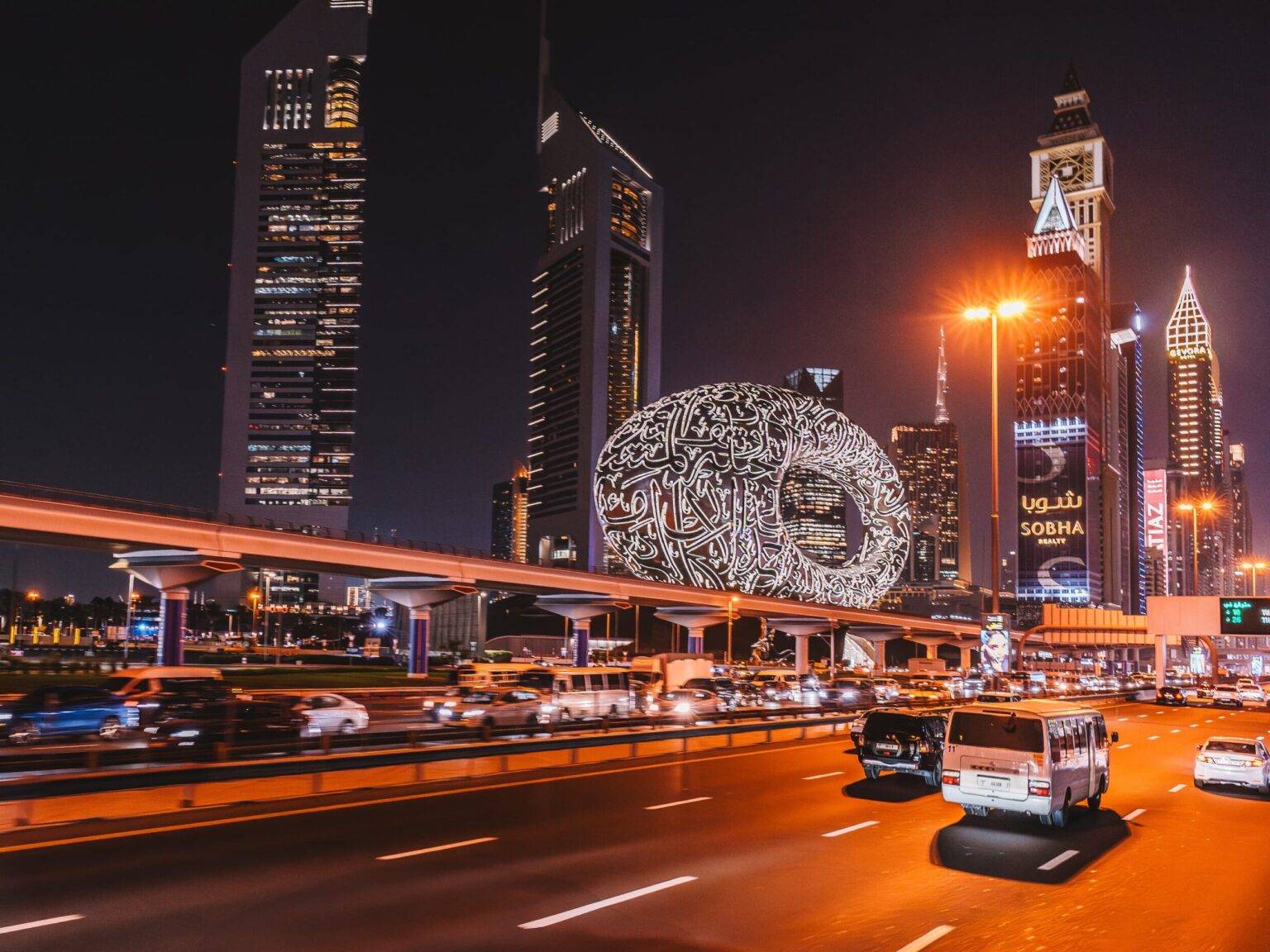 Das Museum of the Future in Dubai bei Nacht hinter einer stark befahrenen Straße und umgeben von Hochhäusern.