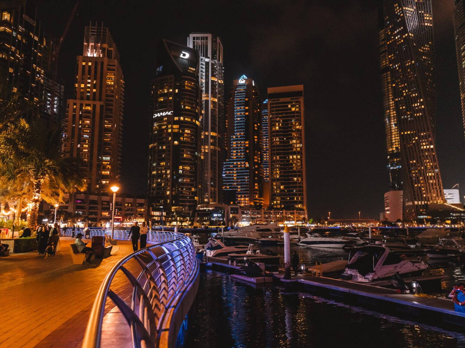 Die Dubai Marina bei Nacht mit vielen Yachten und umgeben von Hochhäusern.
