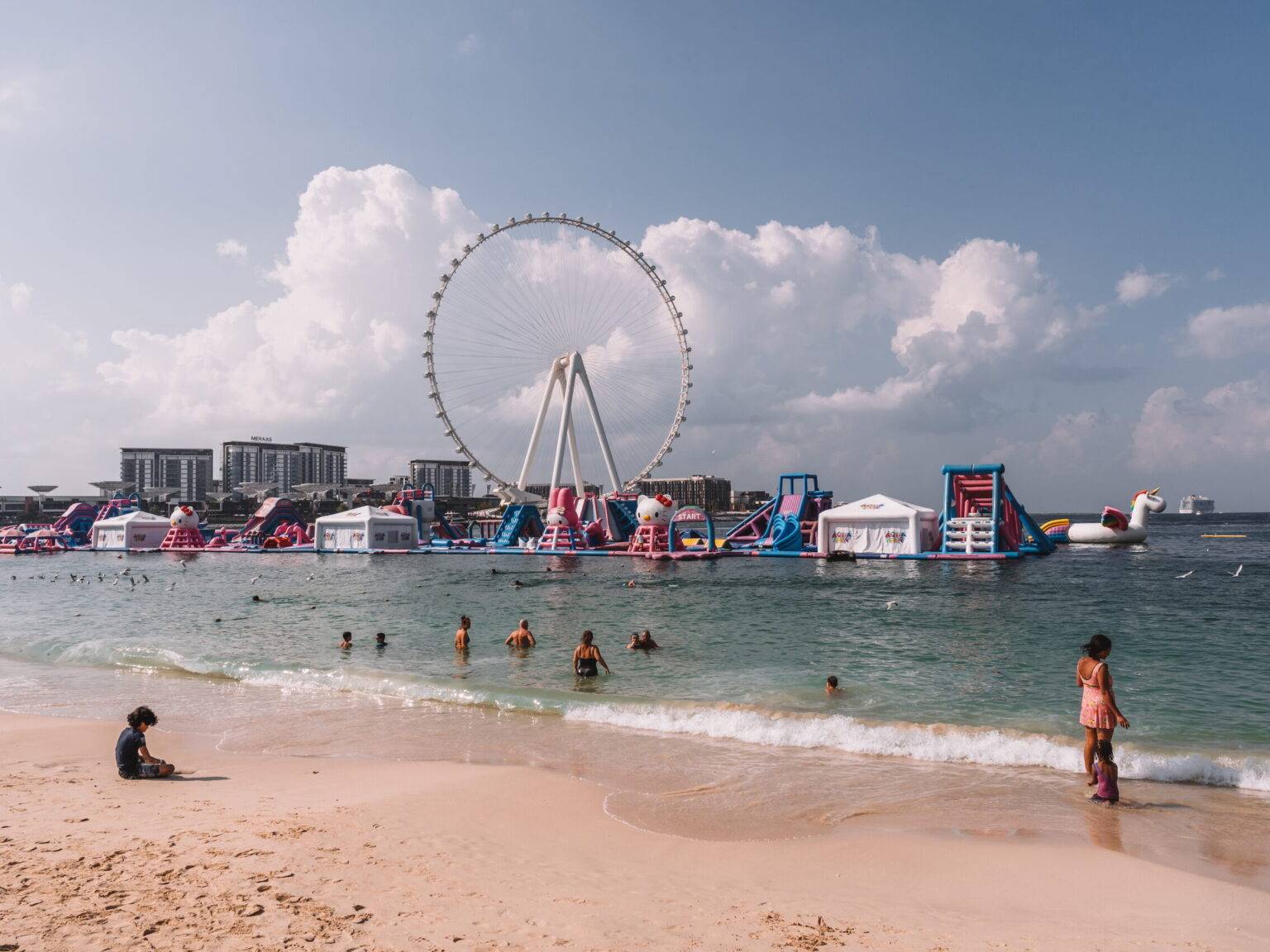 Einige Menschen im Meer am JBR Beach in Dubai mit Hüpfburgen und einem Riesenrad im Hintergrund.