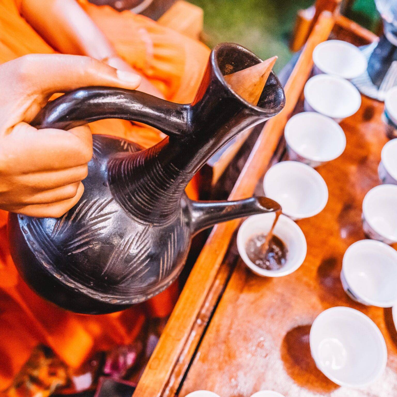 Eine Person gießt Kaffee aus einer Keramikkanne in eine Tasse.