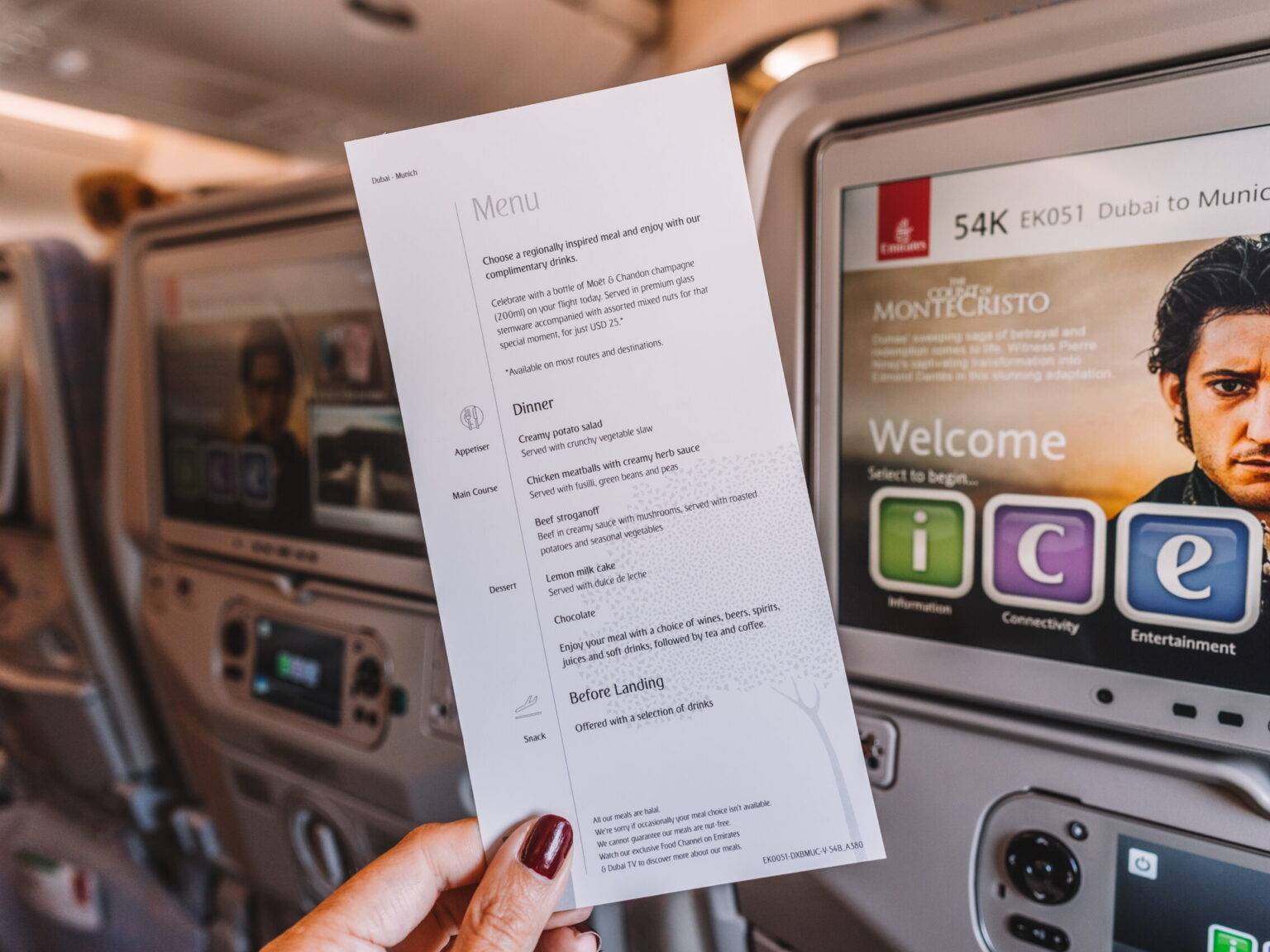 Der Flyer mit dem Board-Menü eines Emirates-Flugs wird vor die Bildschirme auf der Rückseite der Flugzeug-Sitze gehalten.