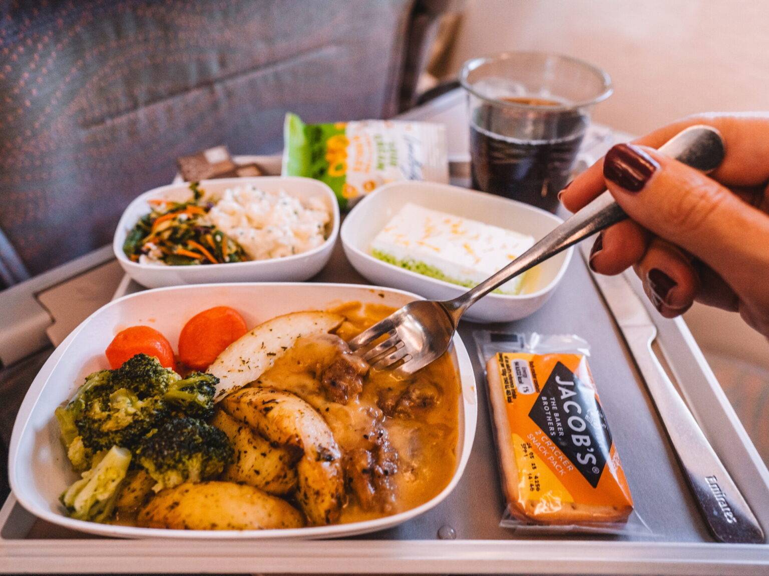 Auf dem Tisch eines Flugzeugsitzes stehen ein Getränk, sowie mehrere Teller und Schalen mit verschiedenen Speisen.
