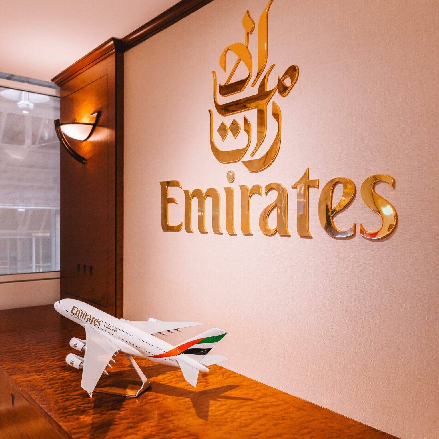 An einer Wand hängt ein großes goldenes Schild mit dem Emirates-Logo. Davor steht das Modell eines Emirates-Flugzeugs.