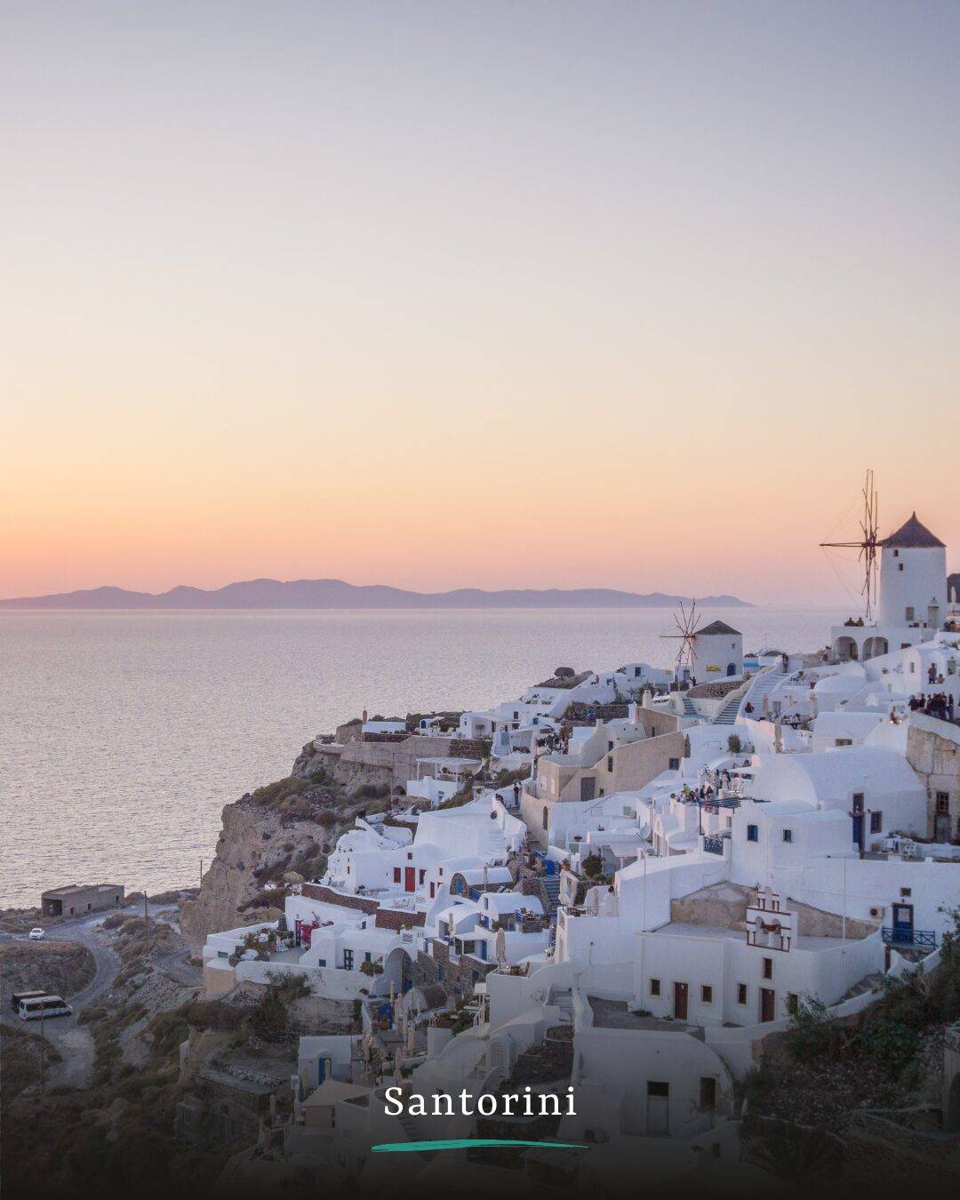 Santorini, ein Ort mit vielen weißen Häusern, die in die Klippen gebaut wurden. Links das Meer und im Hintergrund eine andere Insel. Die Sonne geht gerade unter und der Himmel ist in verschiedenen Orangetönen gefärbt.