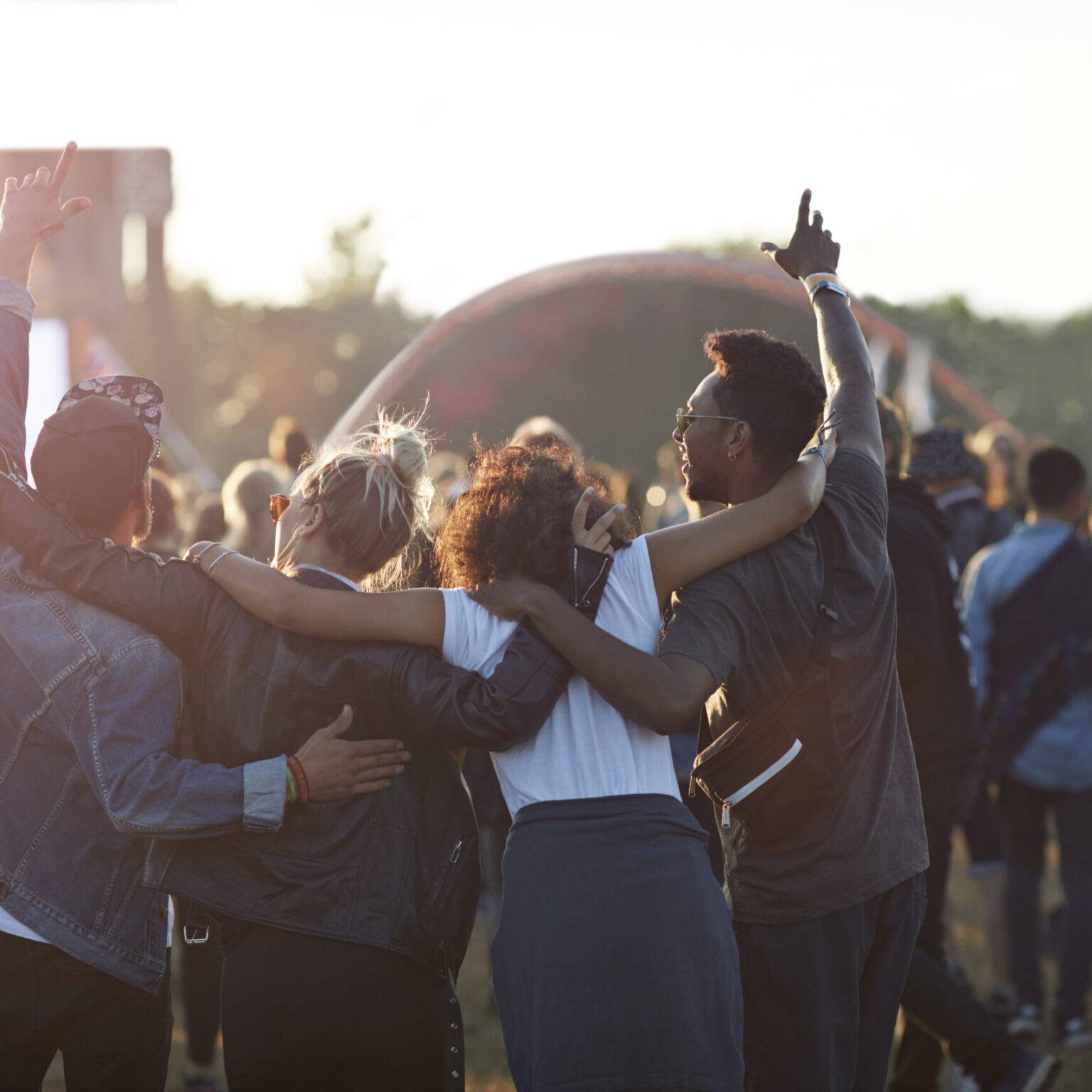 Vier Freunde halten sich feiernd auf einem Festivalgelände in den Armen.