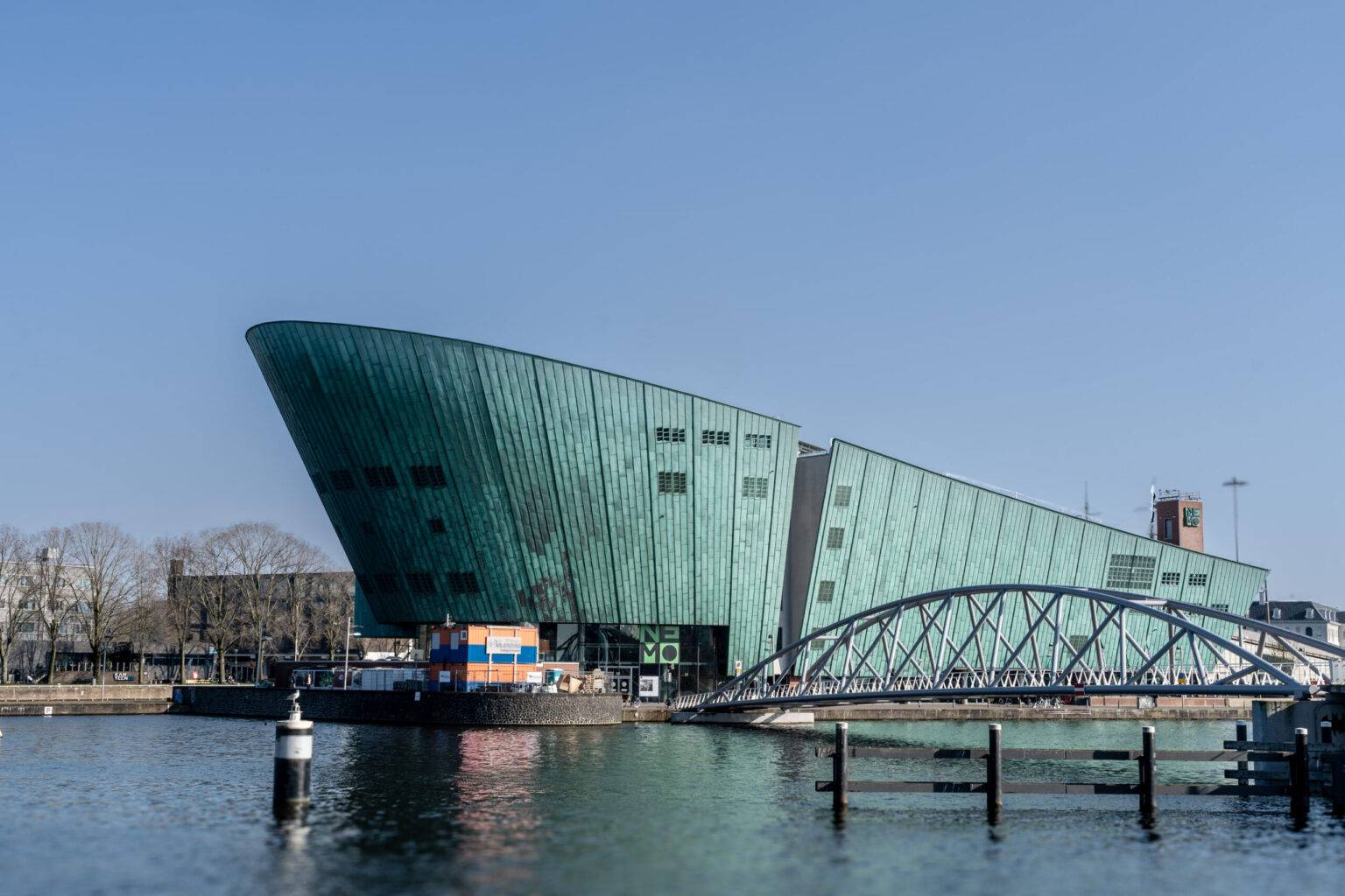 Außenansicht des NEMO Science Museum in Amsterdam mit markanter grünlicher Kupferfassade, umgeben von Wasser.