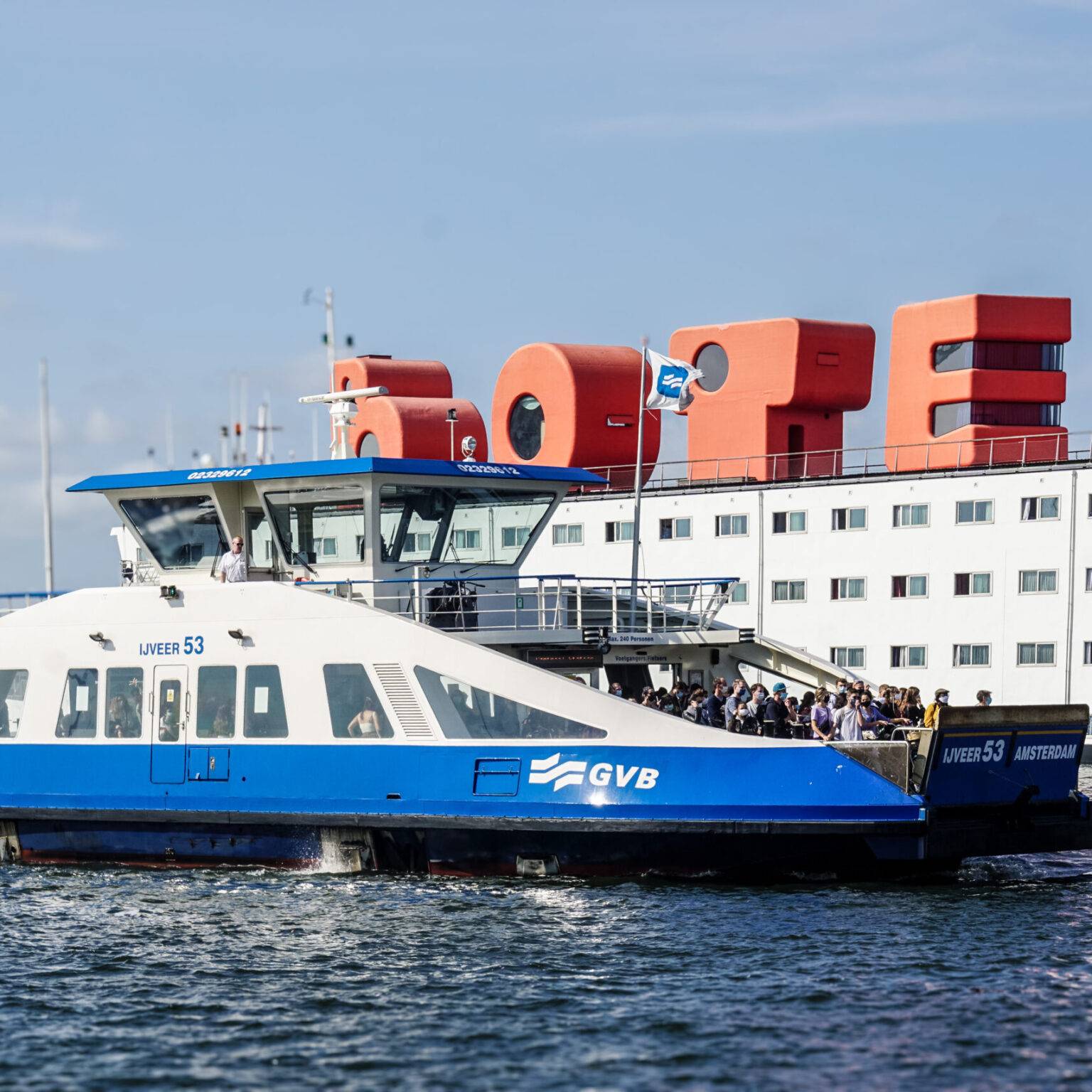Menschen stehen eng beisammen auf einer Fähre, die über den Fluss IJ fährt.